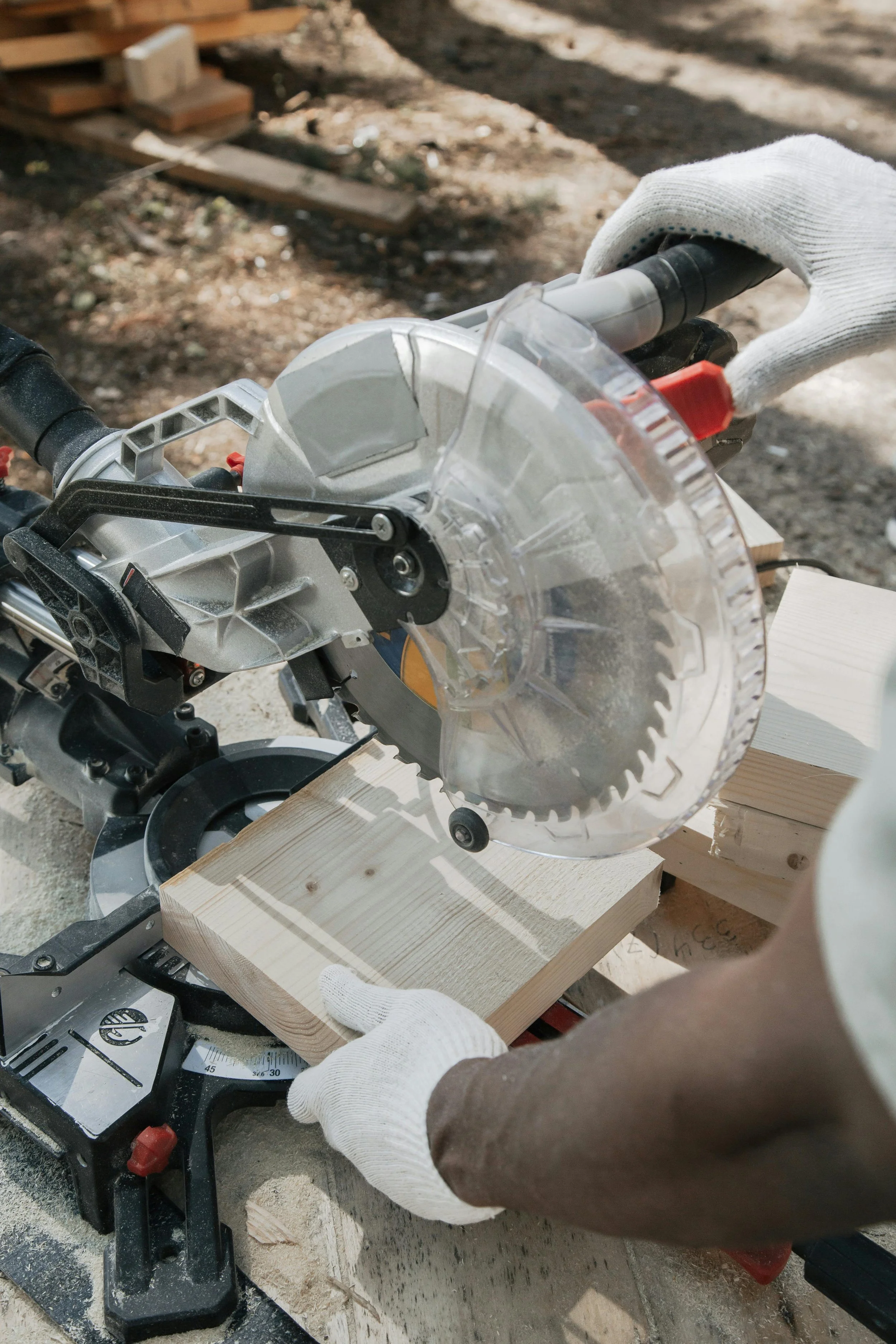 A person operating a miter saw to cut a piece of wood outdoors.