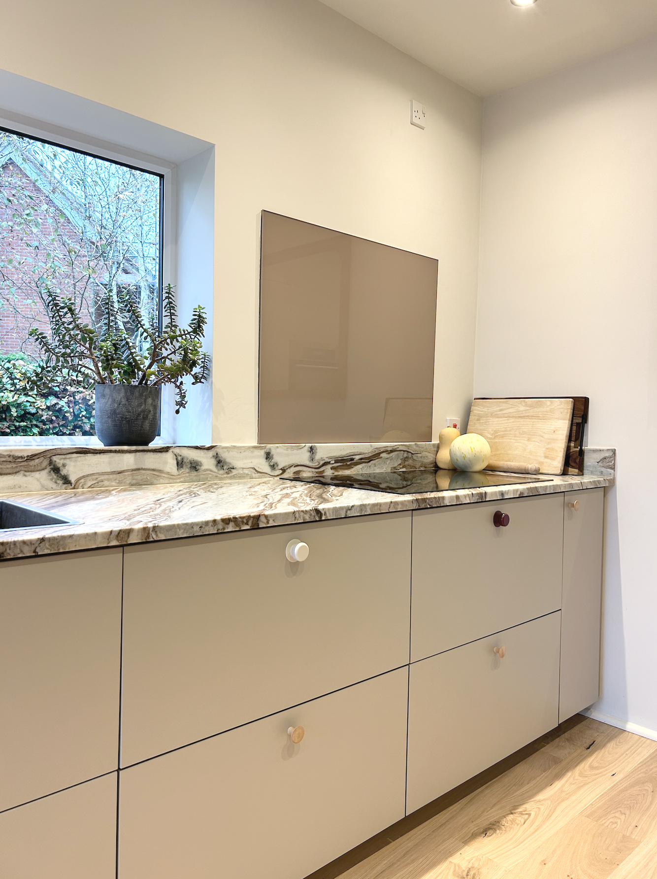 A kitchen countertop with a potted plant near a window, a black cooktop, and some decorative items including two vases and a melon on a cutting board.