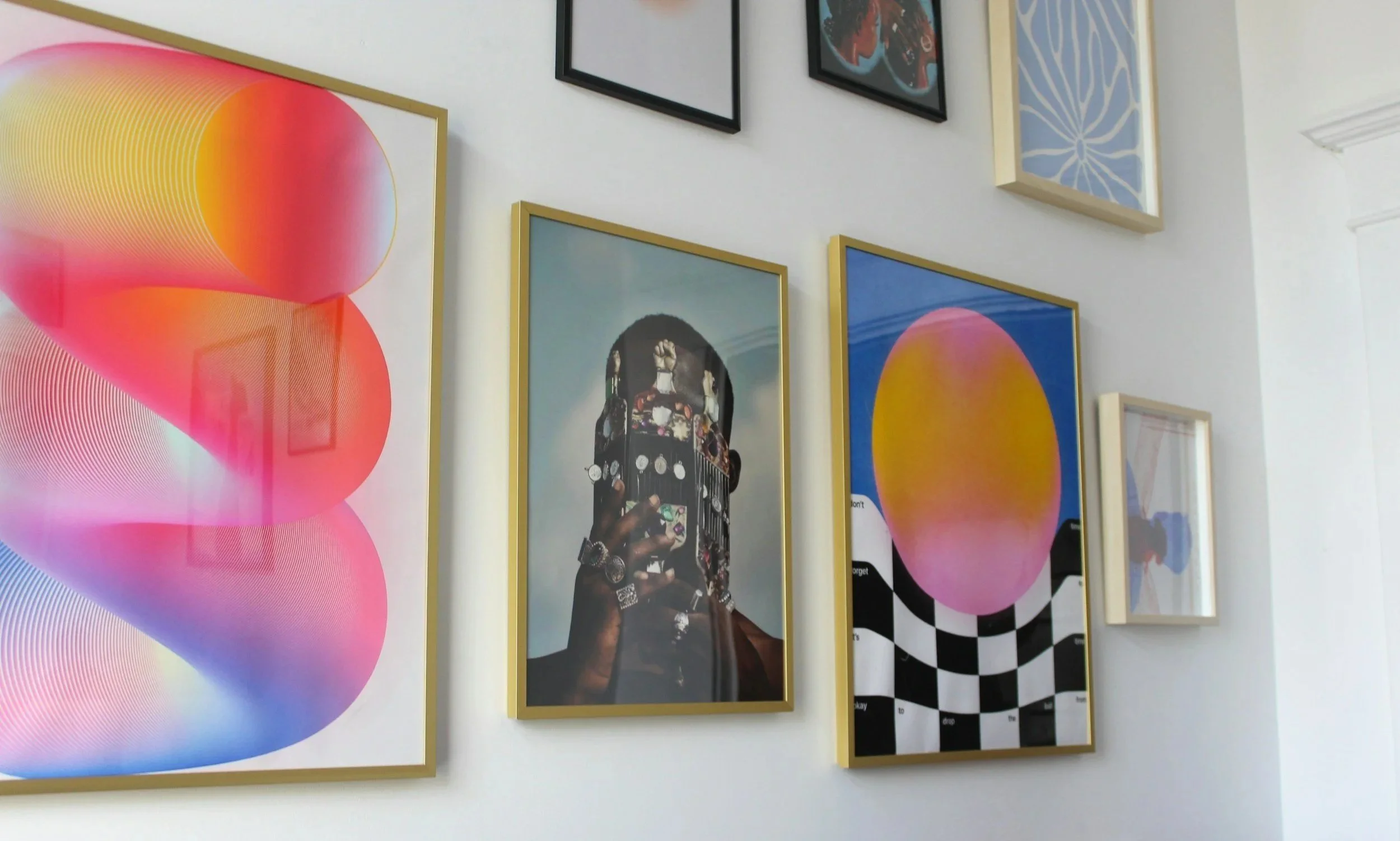 Gallery wall with colorful abstract and portrait art prints in gold frames, including a woman with jewelry representing modern art.