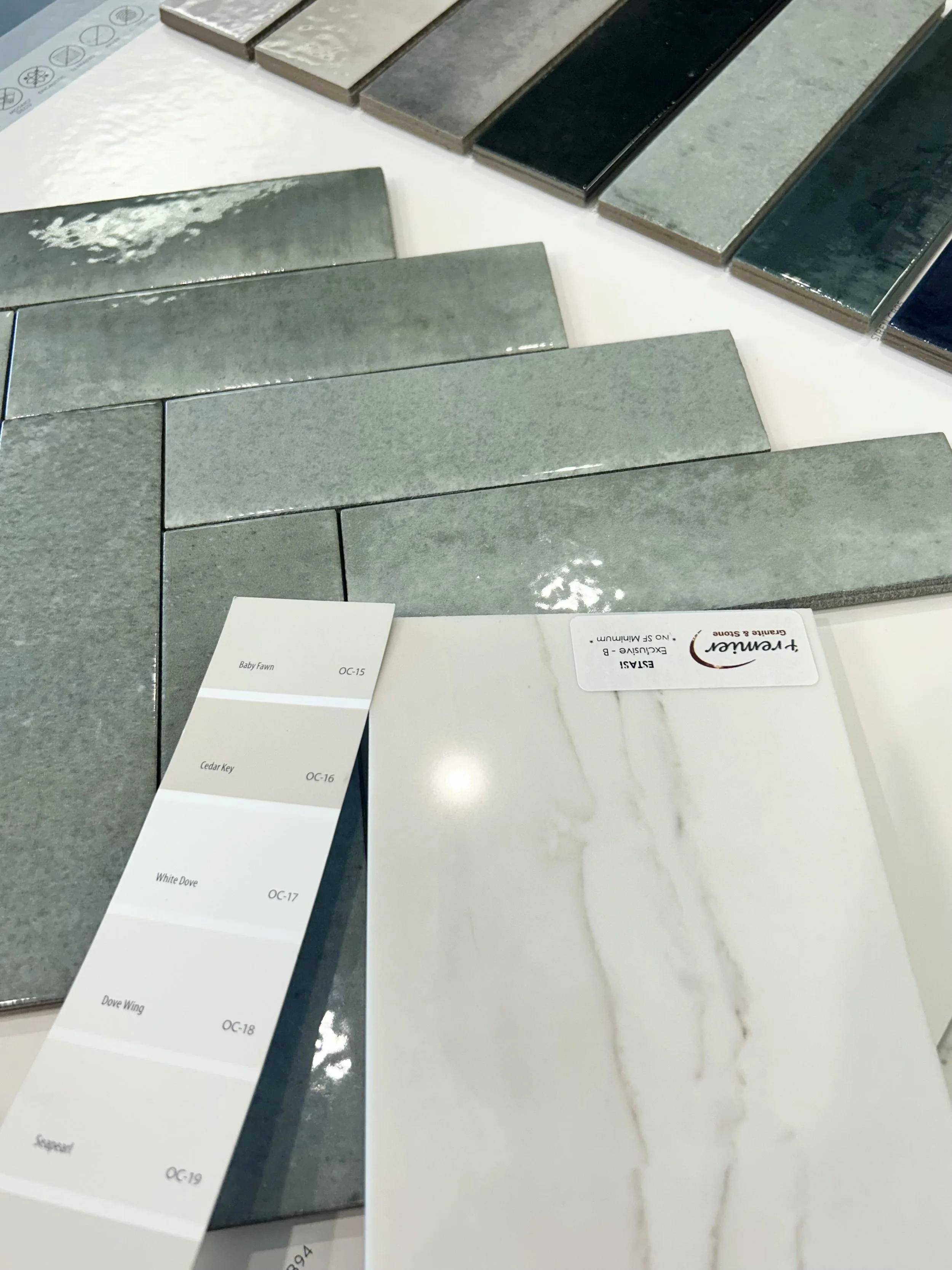 Sample tiles displayed in different shades of gray and beige, arranged in a layout for choosing flooring or wall tiles, with a color chart label and a marble pattern sample.