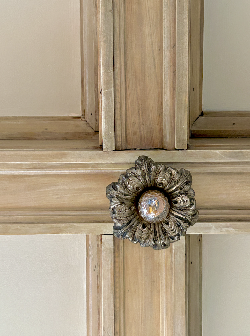 Close-up of a decorative, antique brass doorknob with intricate floral design on a wooden cabinet or door.