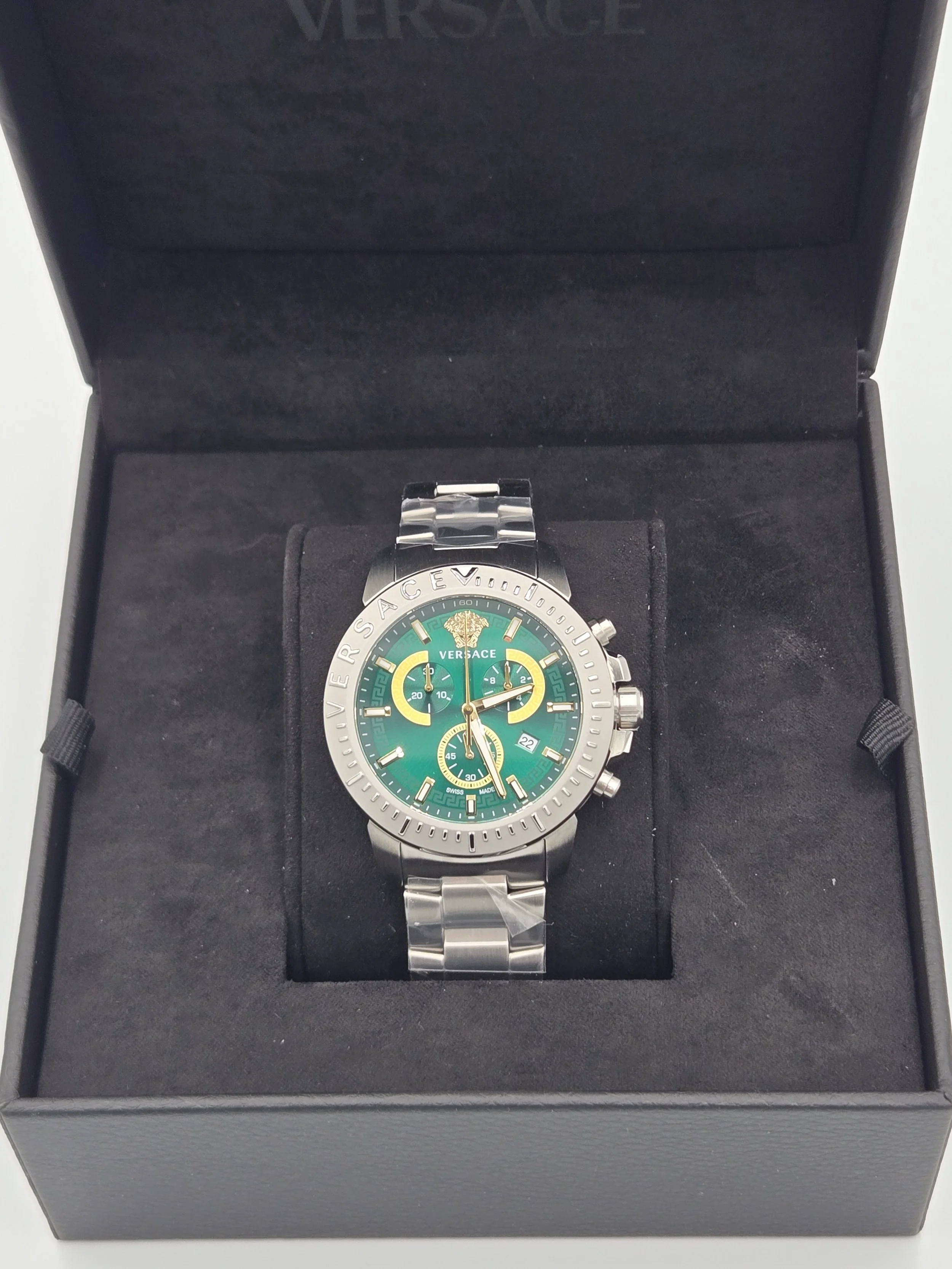 A Versace men's wristwatch with a green dial, silver bezel, and chronograph features, placed inside a black presentation box with a soft interior.