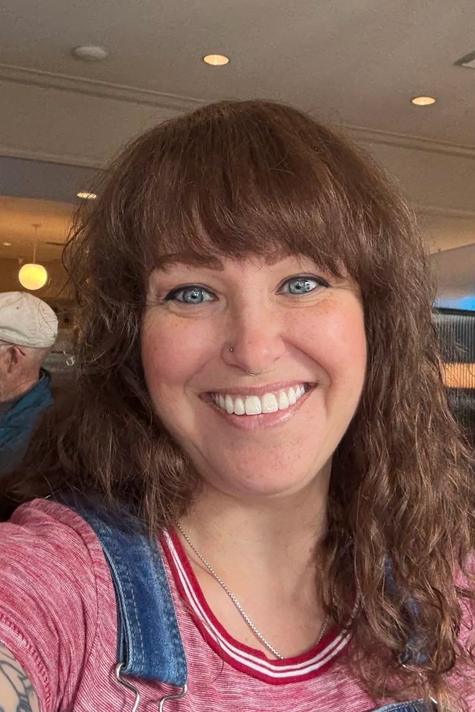 A woman with brown hair and blue eyes smiling in a comfortable and warmly lit setting