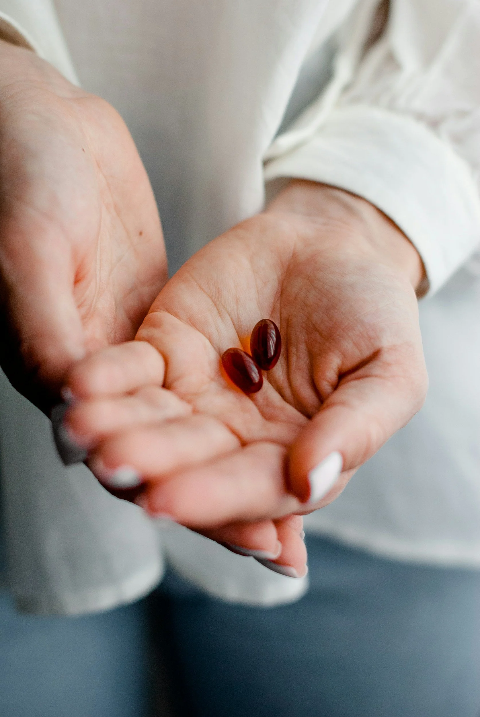 Close-up of a person's hand holding two dark red capsules, with a blurred background.