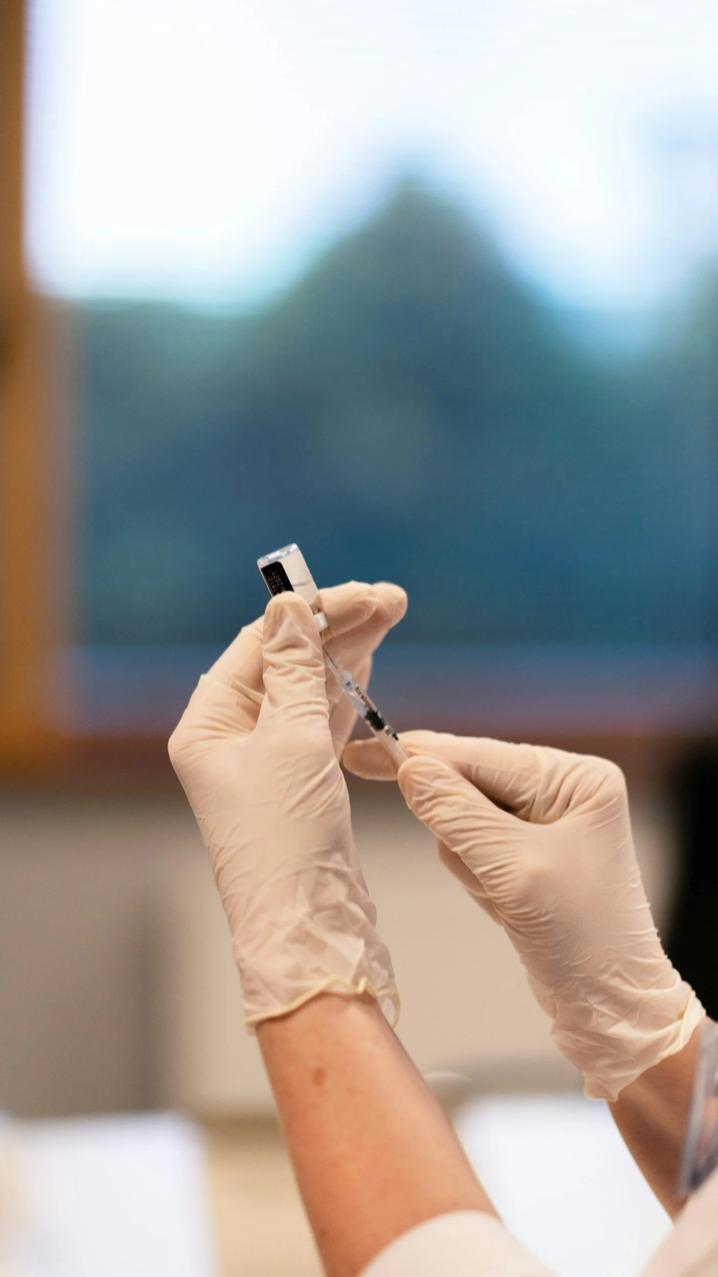 A person wearing latex gloves prepares a syringe with a vaccine or medication, with a blurred background.