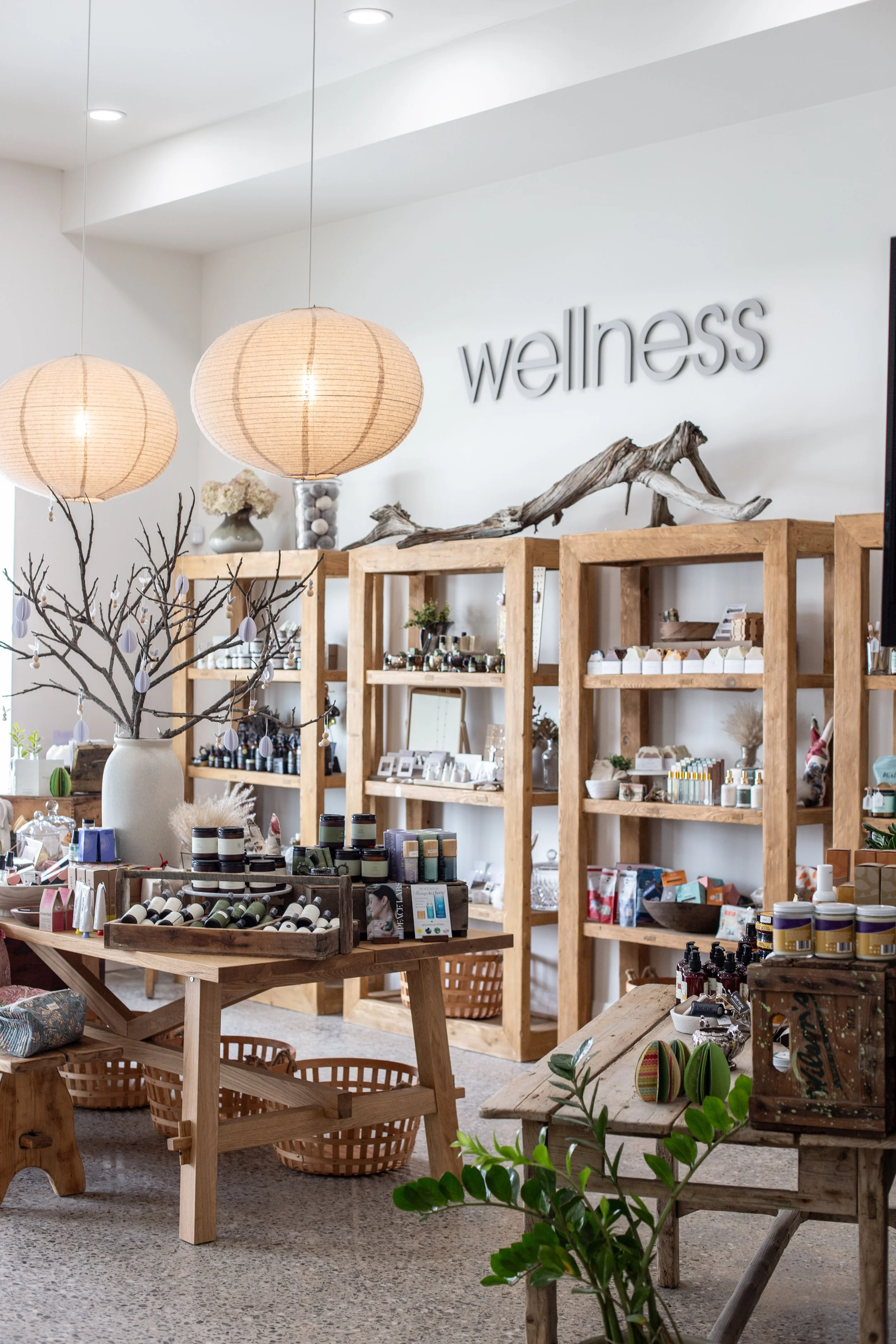 Interior of a wellness store with wooden shelves displaying various products, decorative branches, and hanging paper lantern lights.