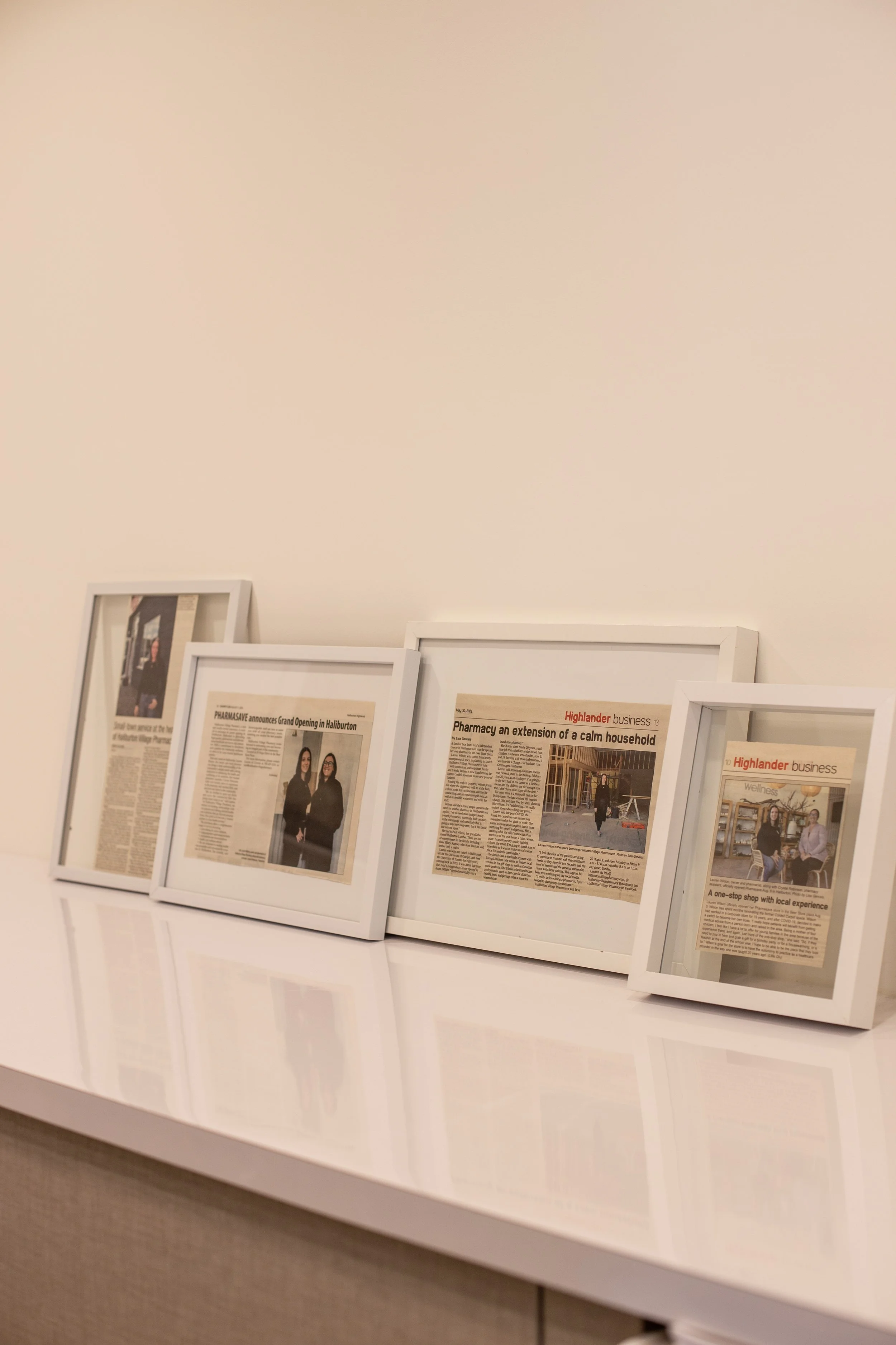 Five framed newspaper articles on a white surface against a plain wall, with their reflections visible on the glossy surface.
