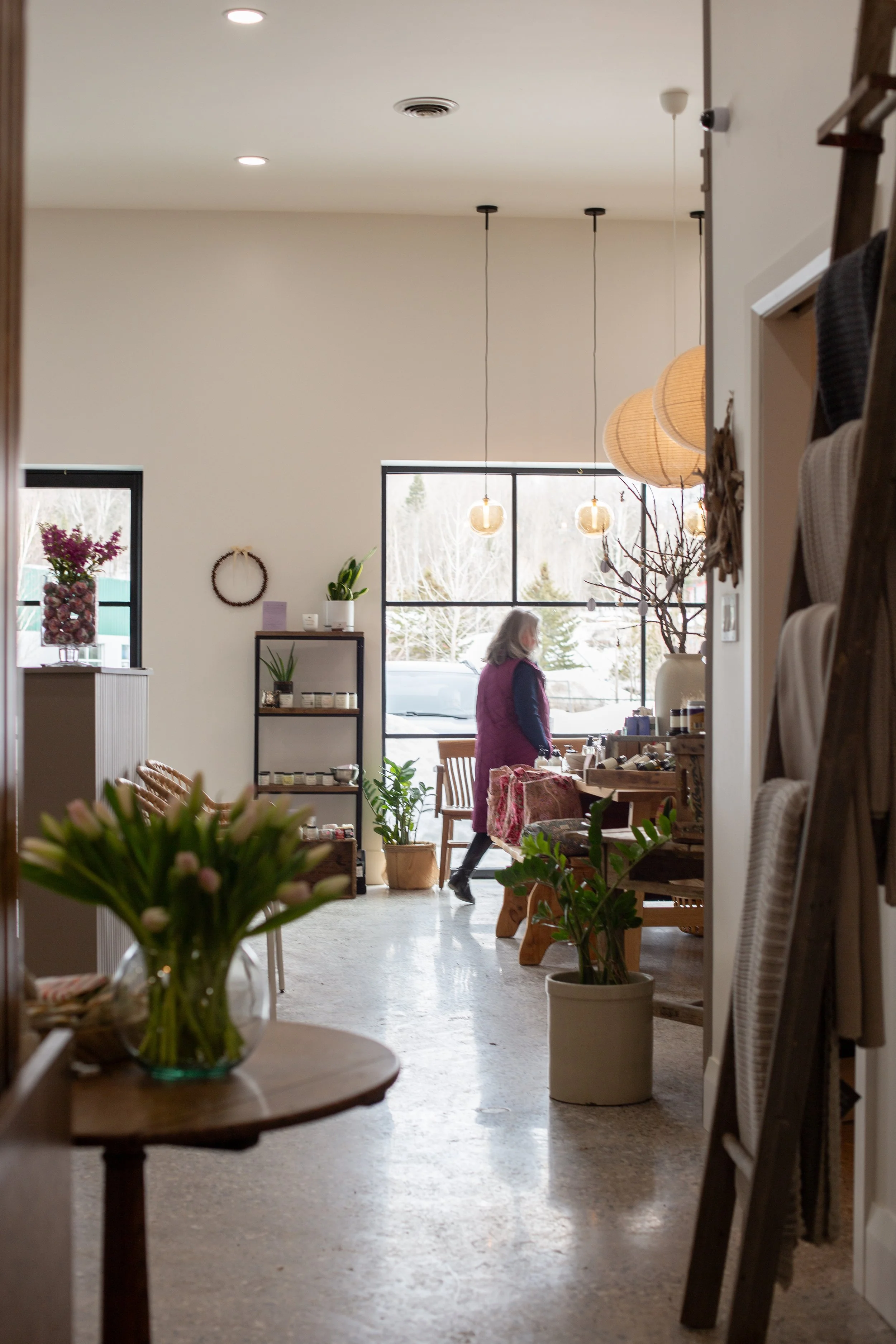 Interior of a boutique or shop with a woman shopping, flowers, plants, and hanging pendant lights.