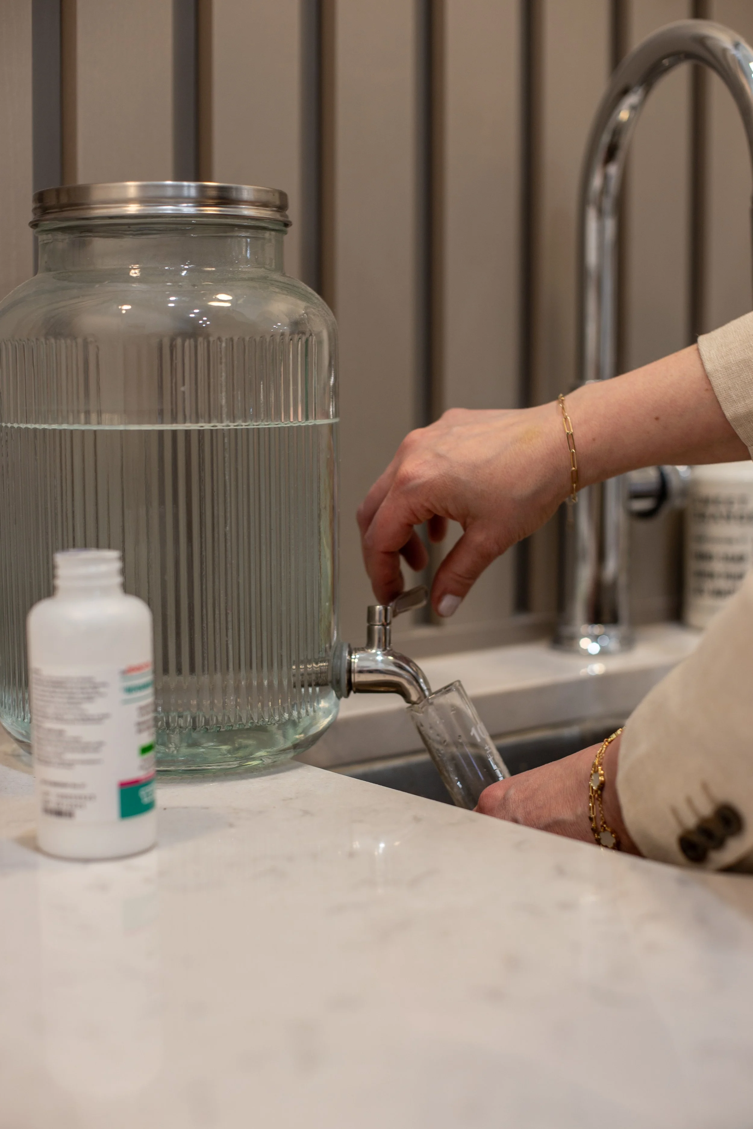 Person filling a glass with water from a water dispenser using a tap.