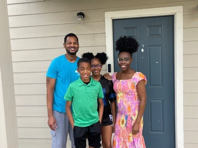 A smiling family standing outside their new home, assisted by Denton Affordable Housing Corporation.