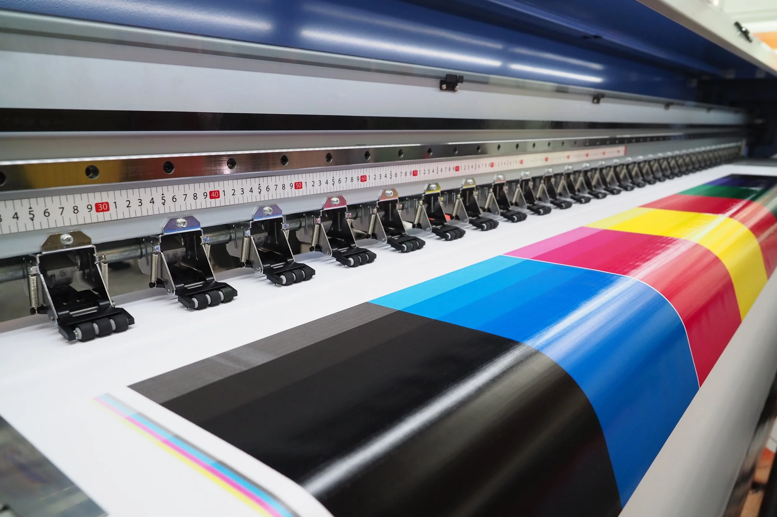 A large printer producing a color test sheet with black, cyan, magenta, yellow, and green color blocks.