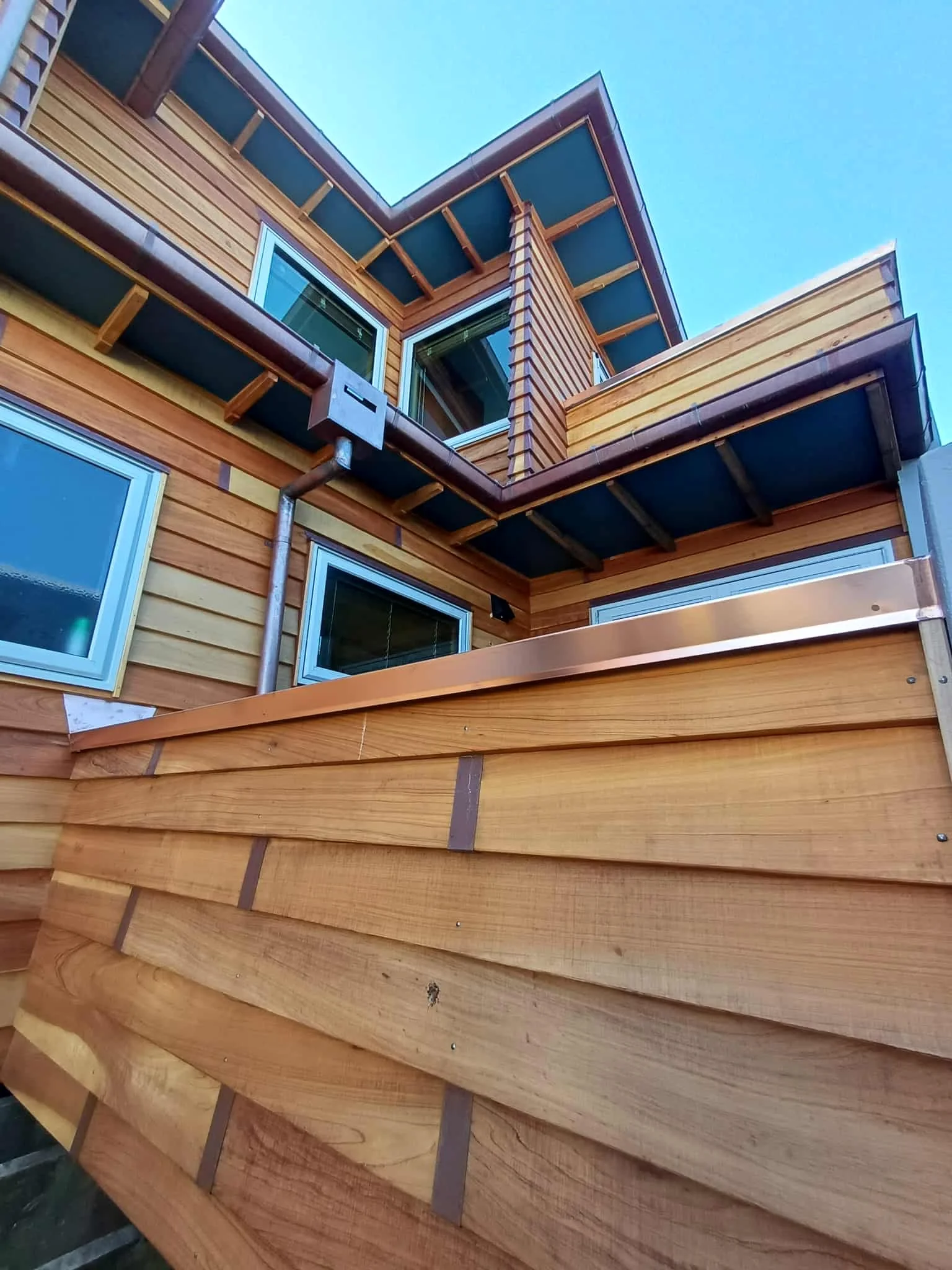 Close-up view of a building's exterior showing wooden siding, windows, and roofing with a blue sky in the background.