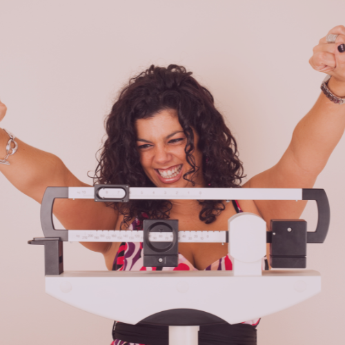 Woman smiling and raising her arms on a weighing scale.