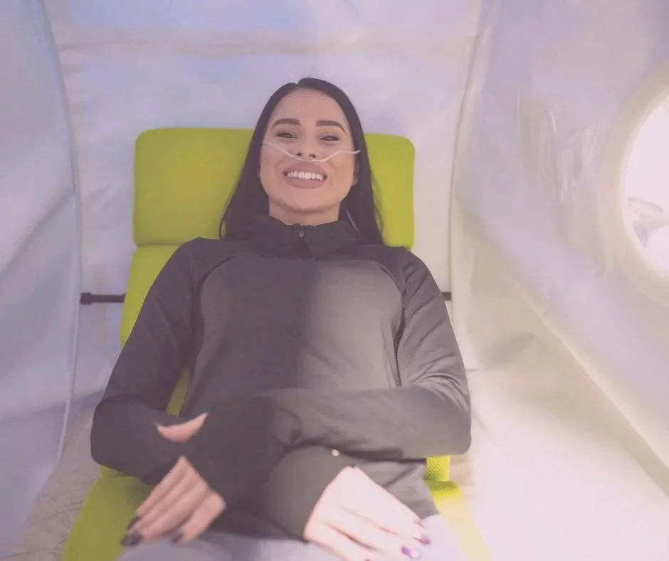 Woman in a hospital bed with an oxygen tube, smiling, in a medical setting.