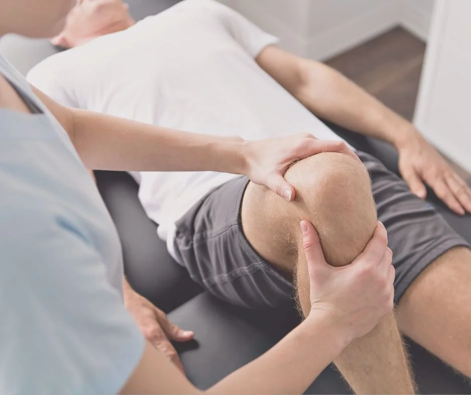 A physical therapist examining a man's knee while he lies on a treatment table.