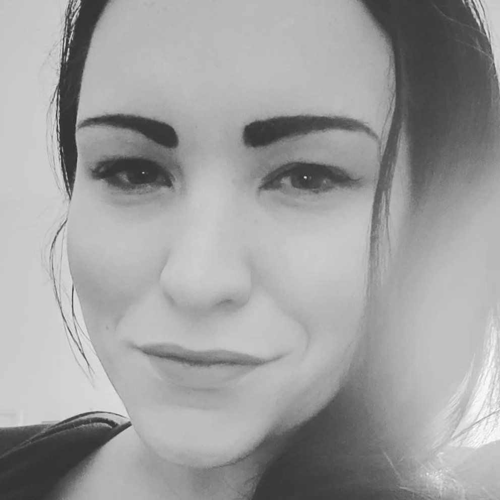 Black and white close-up portrait of a woman with dark hair and makeup, smiling gently.