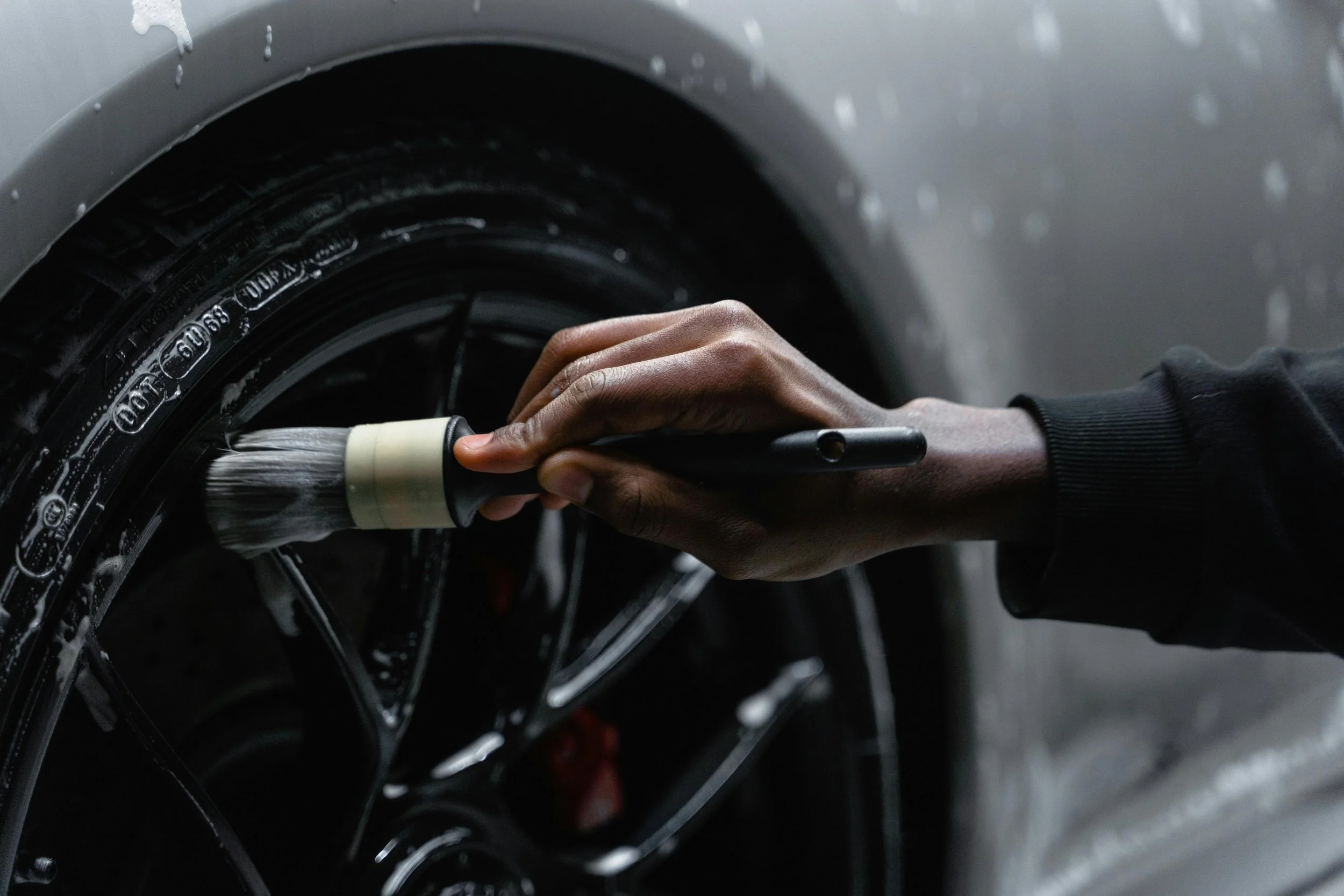 Person cleaning a car wheel with a brush.