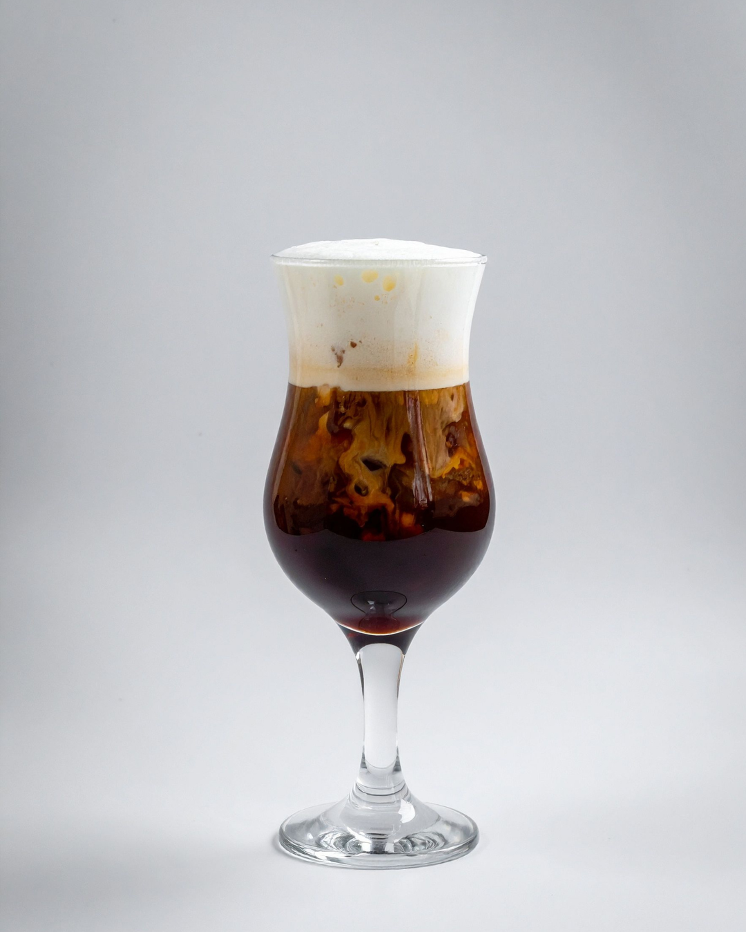 Verre de café froid avec mousse blanche sur le dessus, présenté dans un verre long et élégant.