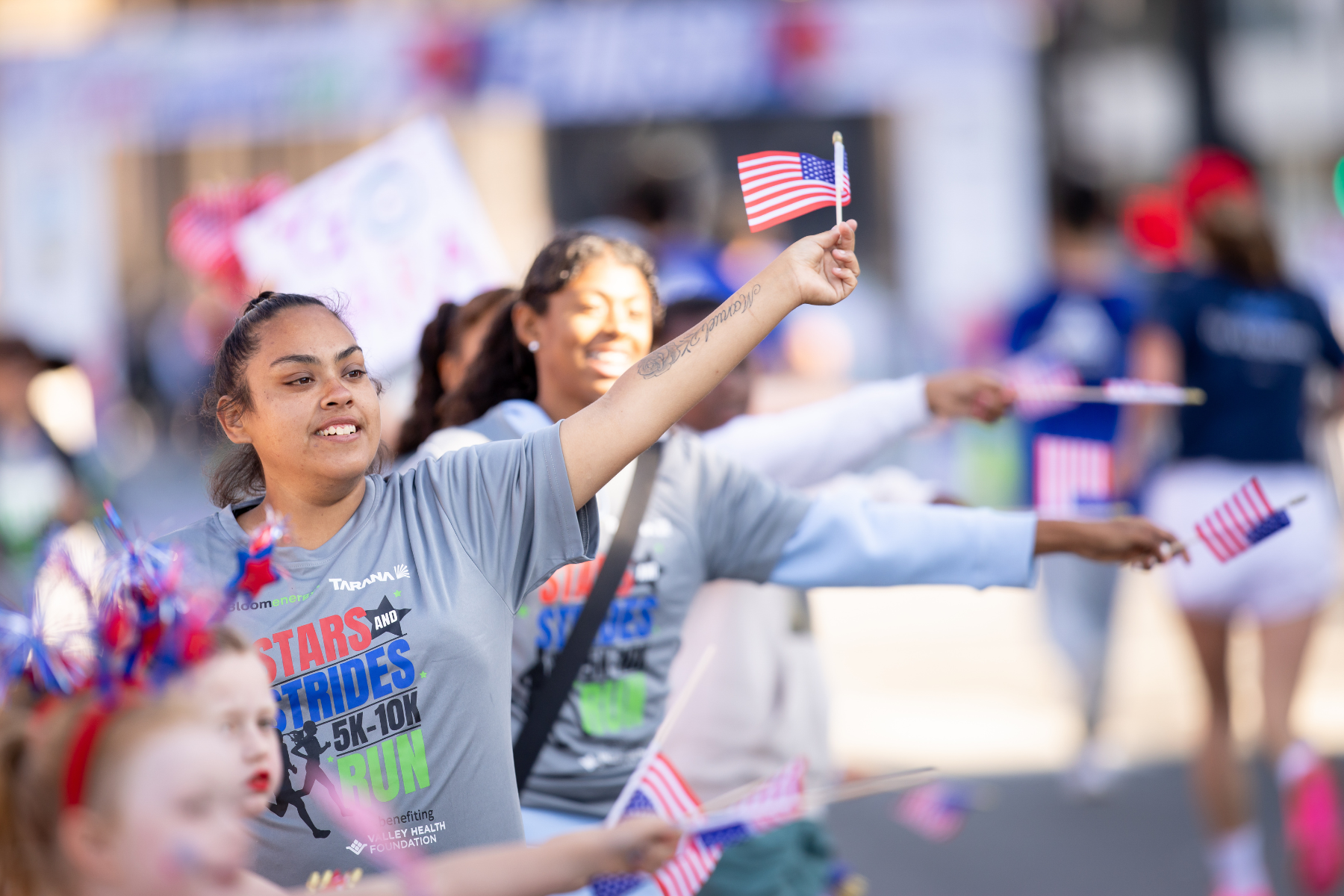 Group of women and children participating in a patriotic parade, waving small American flags, celebrating in a festive outdoor setting.