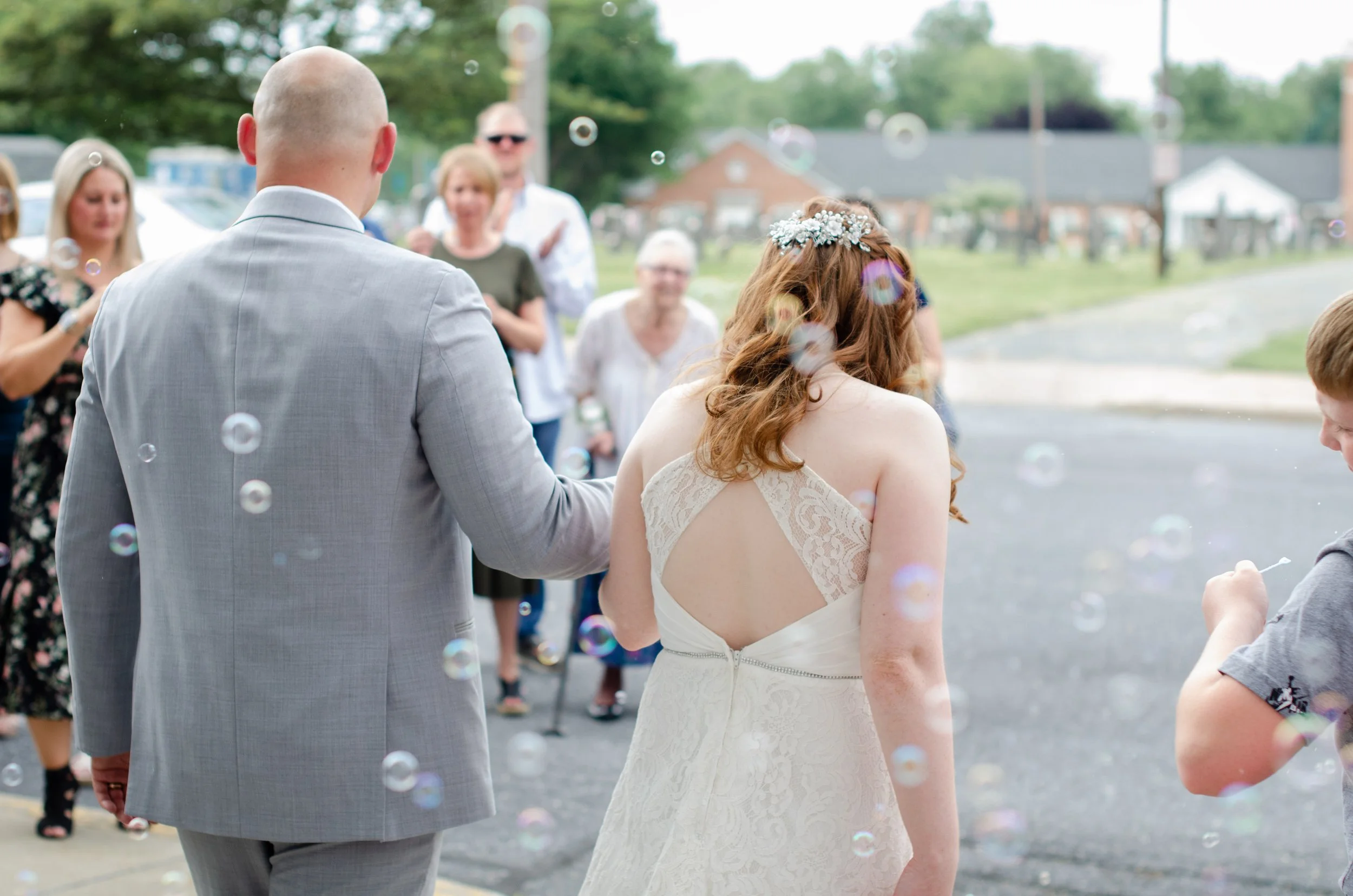 Bride and groom walking outside, surrounded by friends and family, during a wedding celebration with soap bubbles floating in the air.
