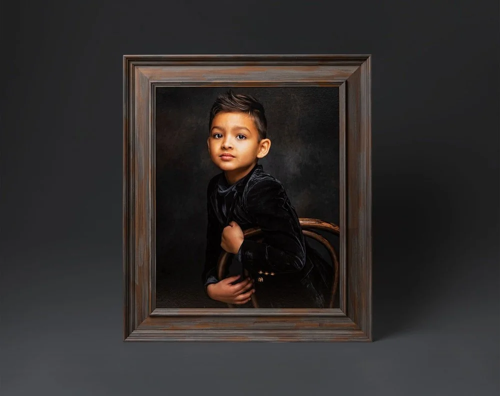 Framed portrait of a young boy with dark hair, sitting on a chair against a black background, wearing a black velvet jacket.