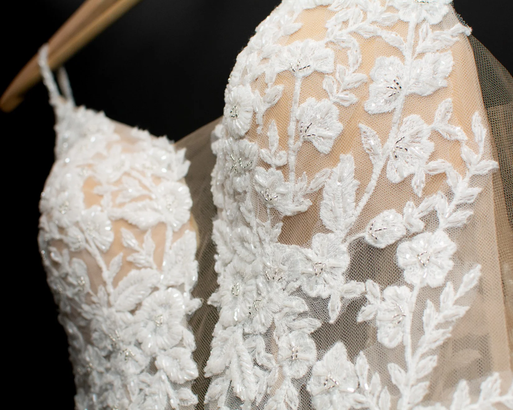 Close-up of an off-white, embroidered wedding dress with floral lace applique and beadwork.