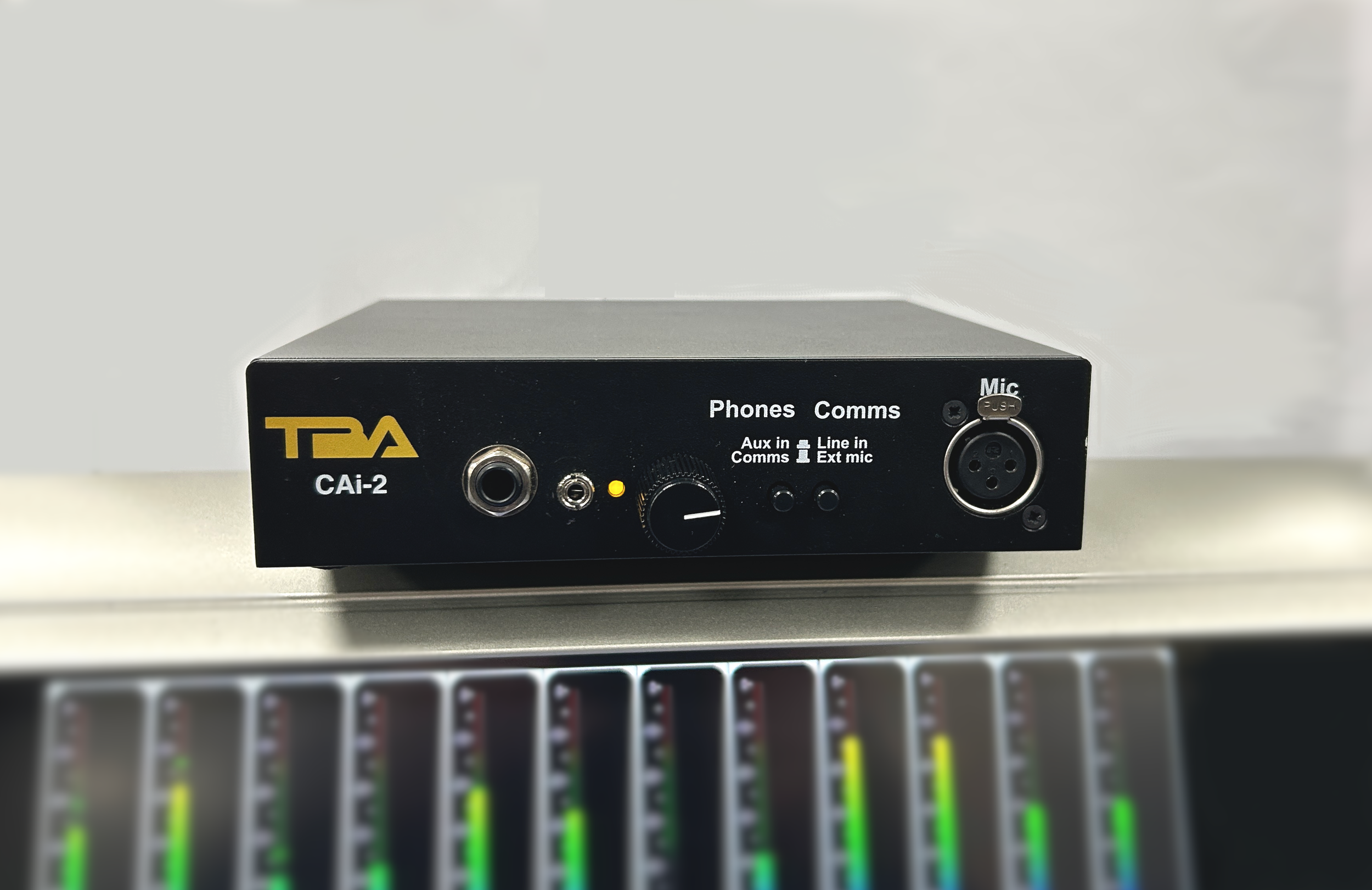 A black audio interface device with various input and output ports, including headphones, microphone, line input, and control knobs, placed on a desk.