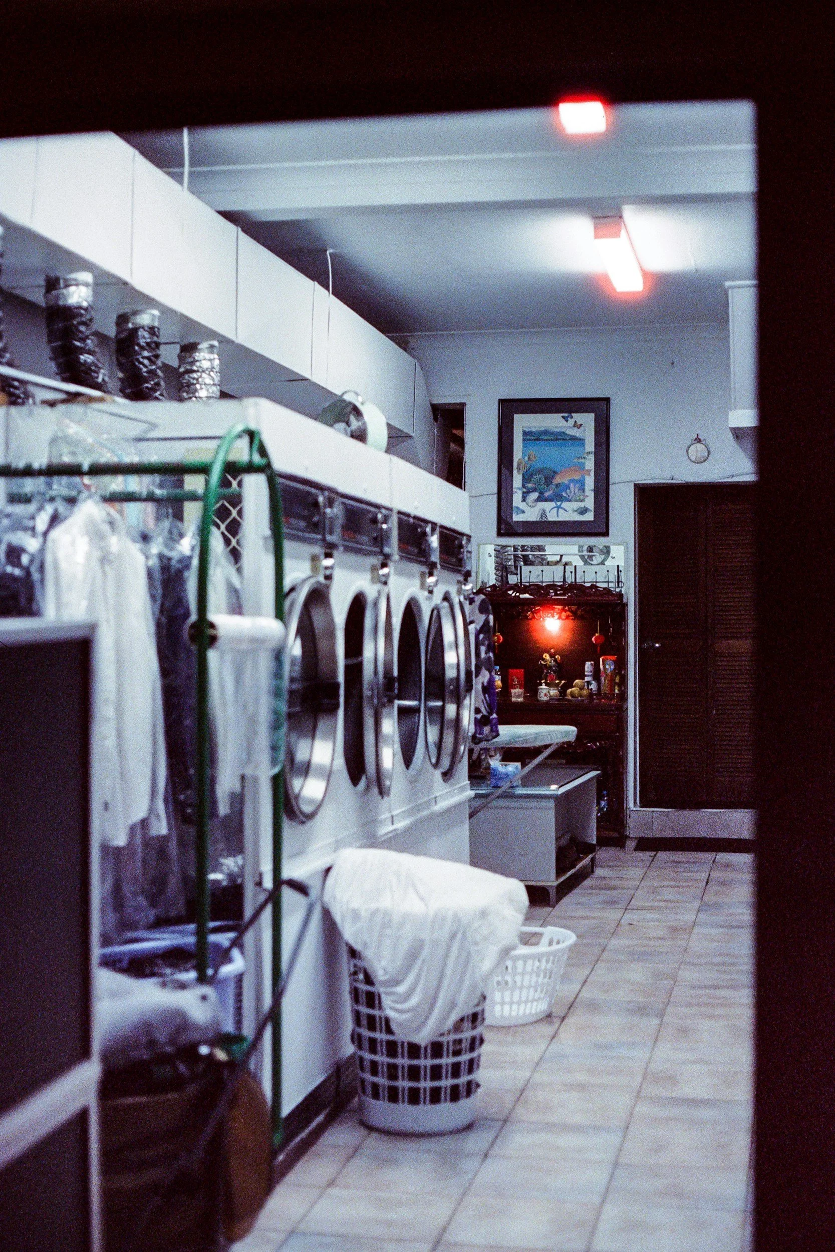 View through a small window into a laundromat with washing machines, laundry baskets, and some kitchen items in the background.