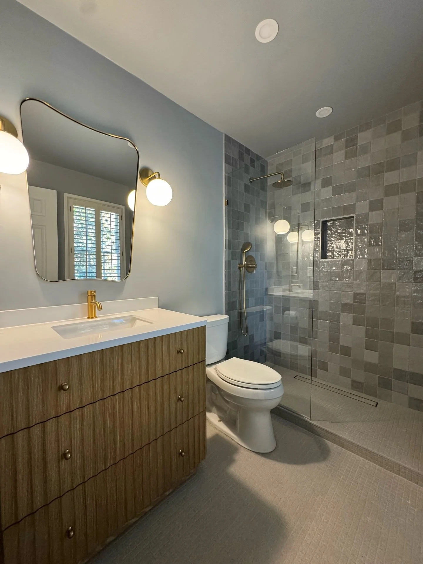Very happy with the result of this guest bathroom renovation🚿

We added a subtle mid-century twist with warm walnut cabinetry, sculptural mirror lines, and brushed brass details  all balanced by soft blue/gray porcelain tile for a serene, modern fee