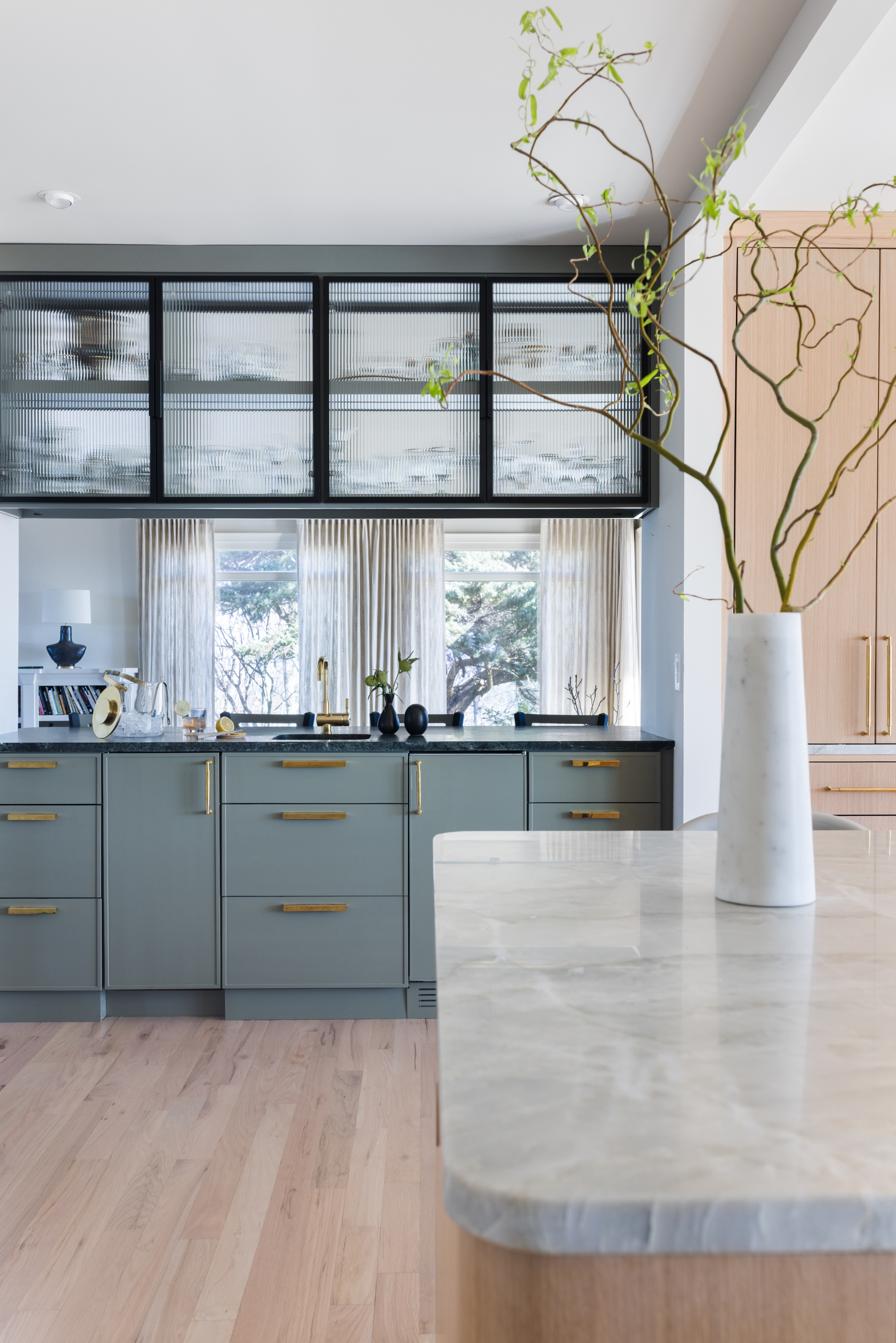 Modern kitchen interior with a white marble vase holding a large plant with twisting green stems placed on a light-colored countertop.