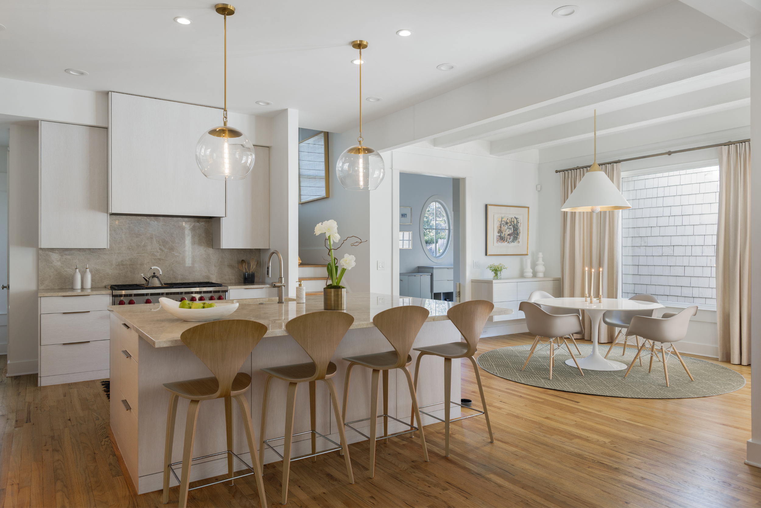 Open-concept kitchen and dining area with white cabinetry, wooden flooring, a kitchen island with barstools, and a round dining table with chairs on a green rug, all in a modern, minimalist style.