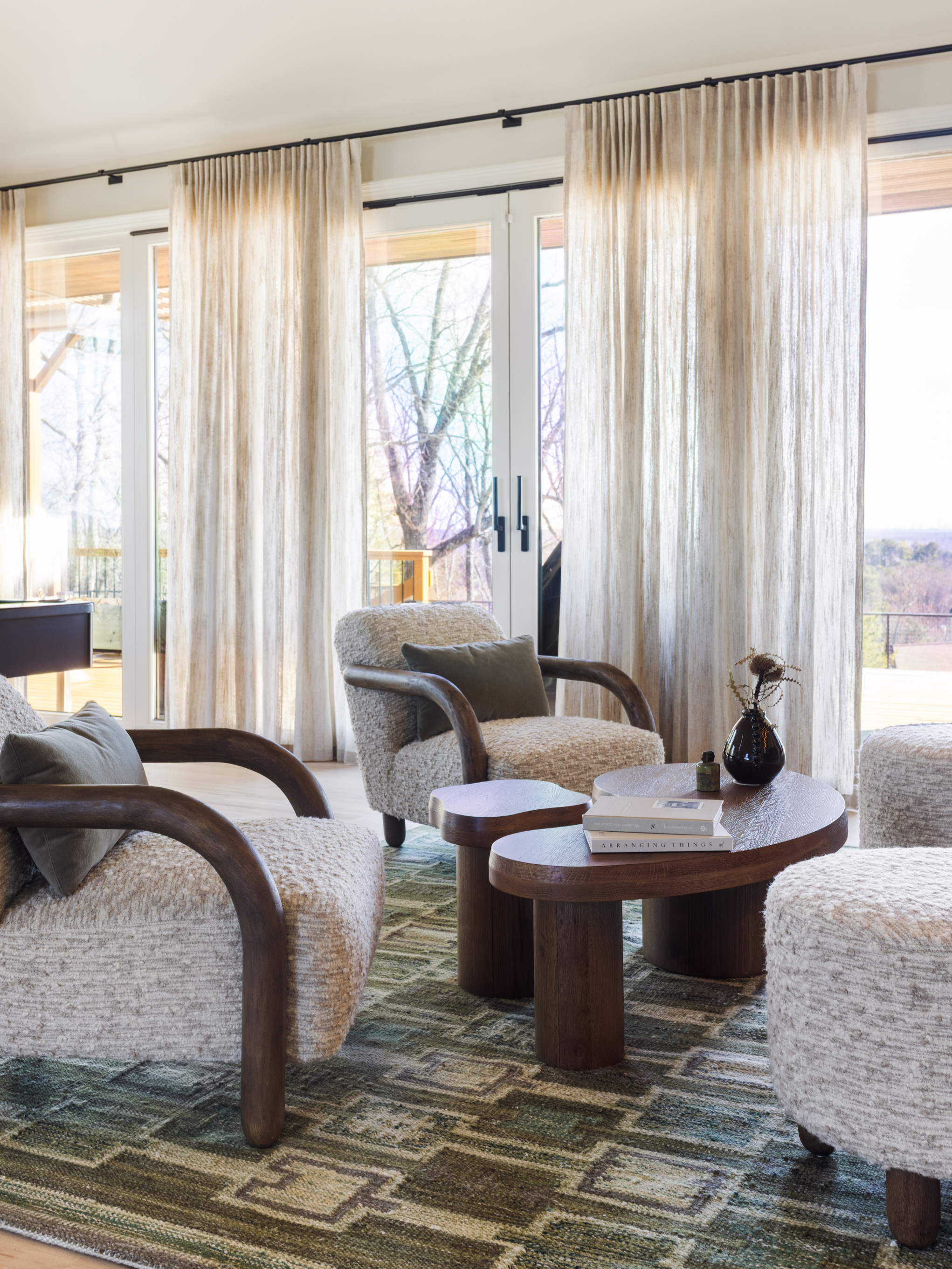 Living room with beige curtains, a sliding glass door, and wooden furniture including armchairs and a coffee table, decorated with books and a vase