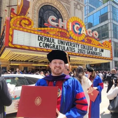 Ben McAdams holds his law school degree and smiles in front of the Chicago theatre.