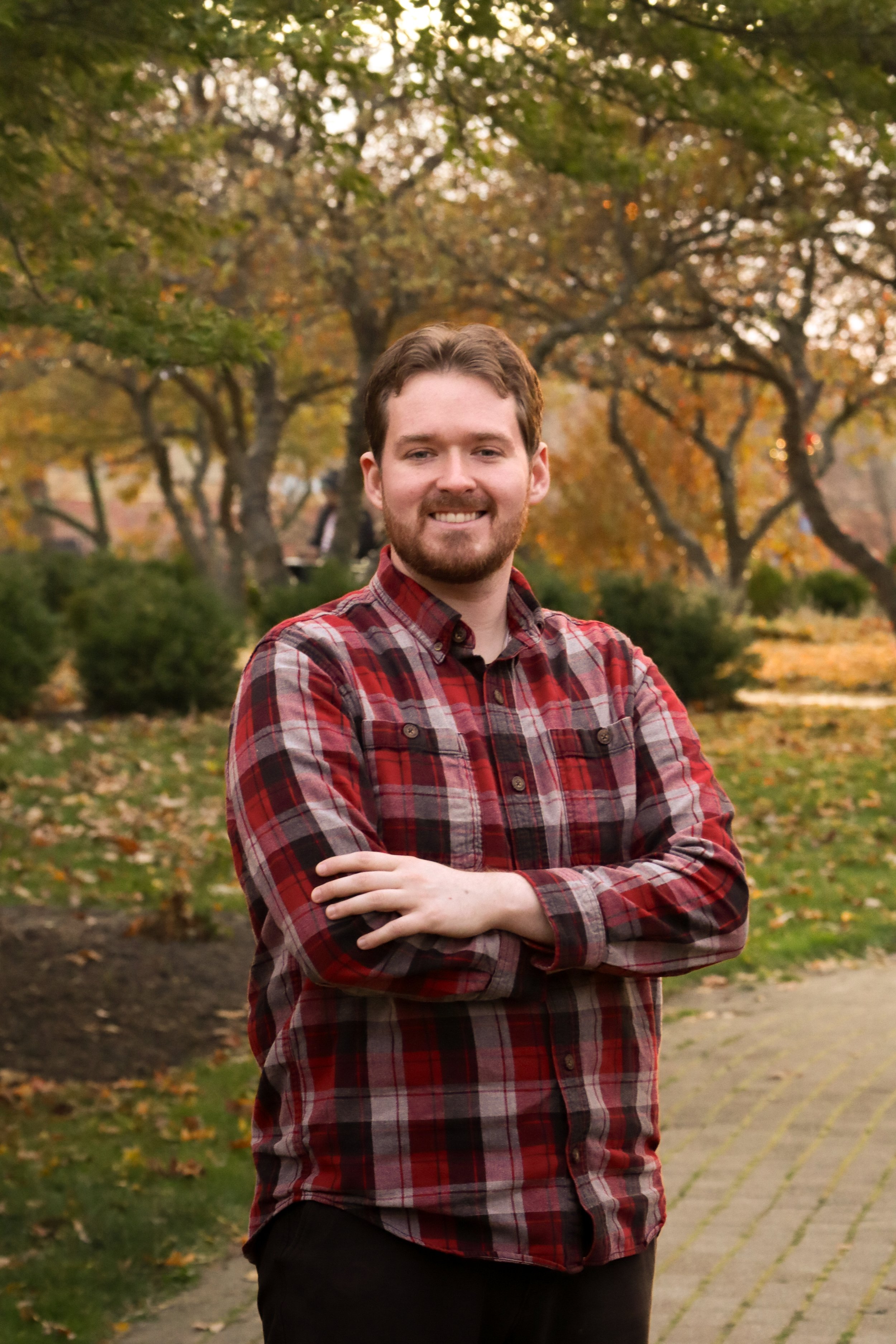 Ben McAdams, standing with his arms crossed, smiles in front of a park.