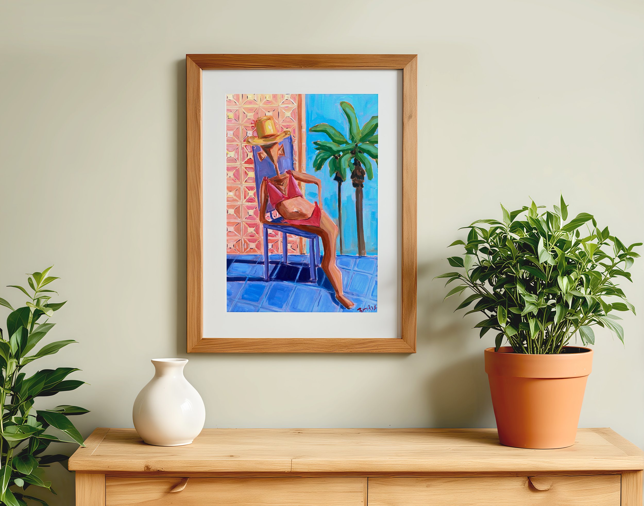 A framed painting of a woman in a red swimsuit with a hat, sitting on a chair next to a tropical palm tree, with a patterned wall and blue floor in the background. The painting hangs on a light-colored wall, with a wooden shelf below holding a white vase and a large potted green plant.
