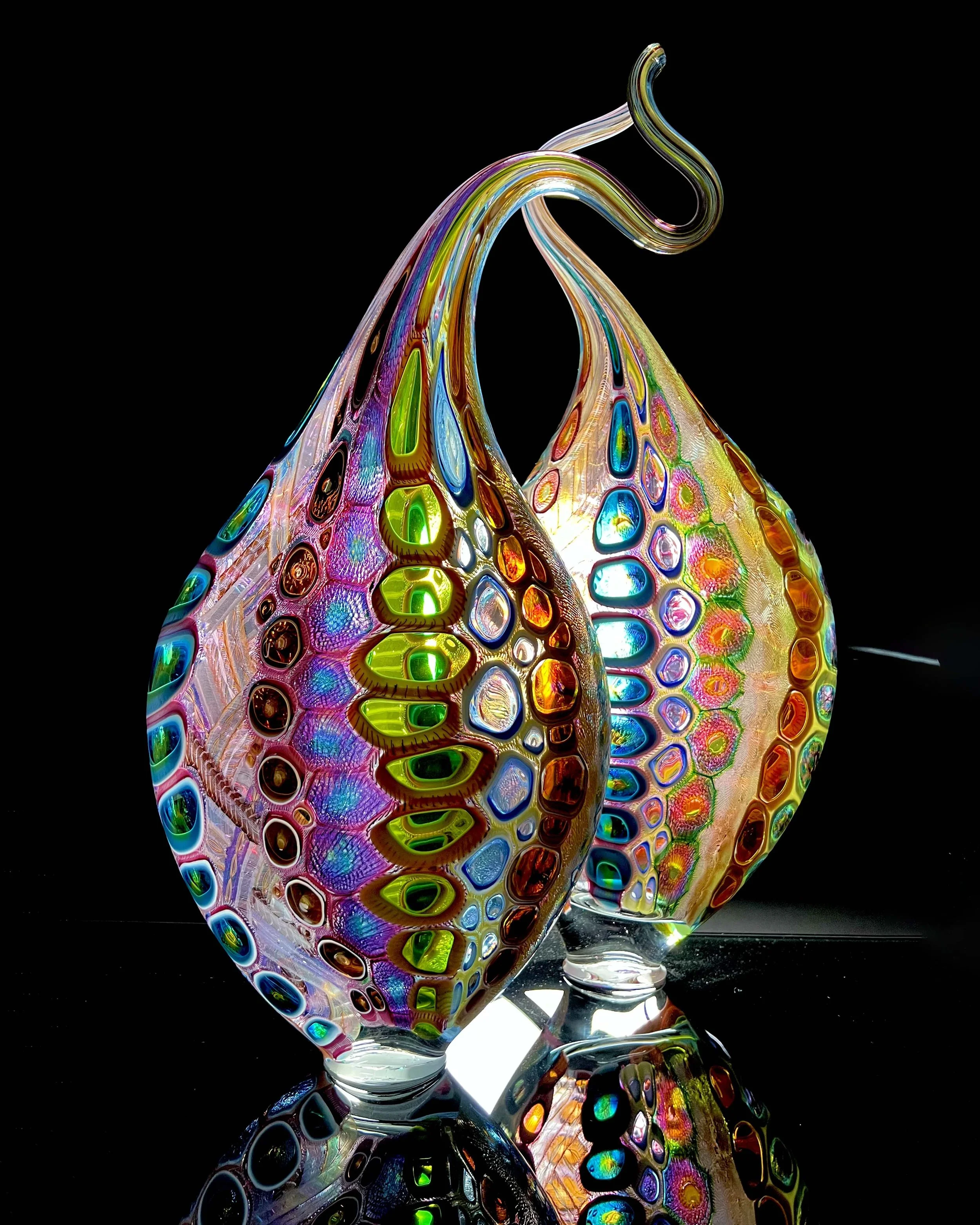 Two colorful, patterned glass vases with swirling designs reflecting on a black surface.