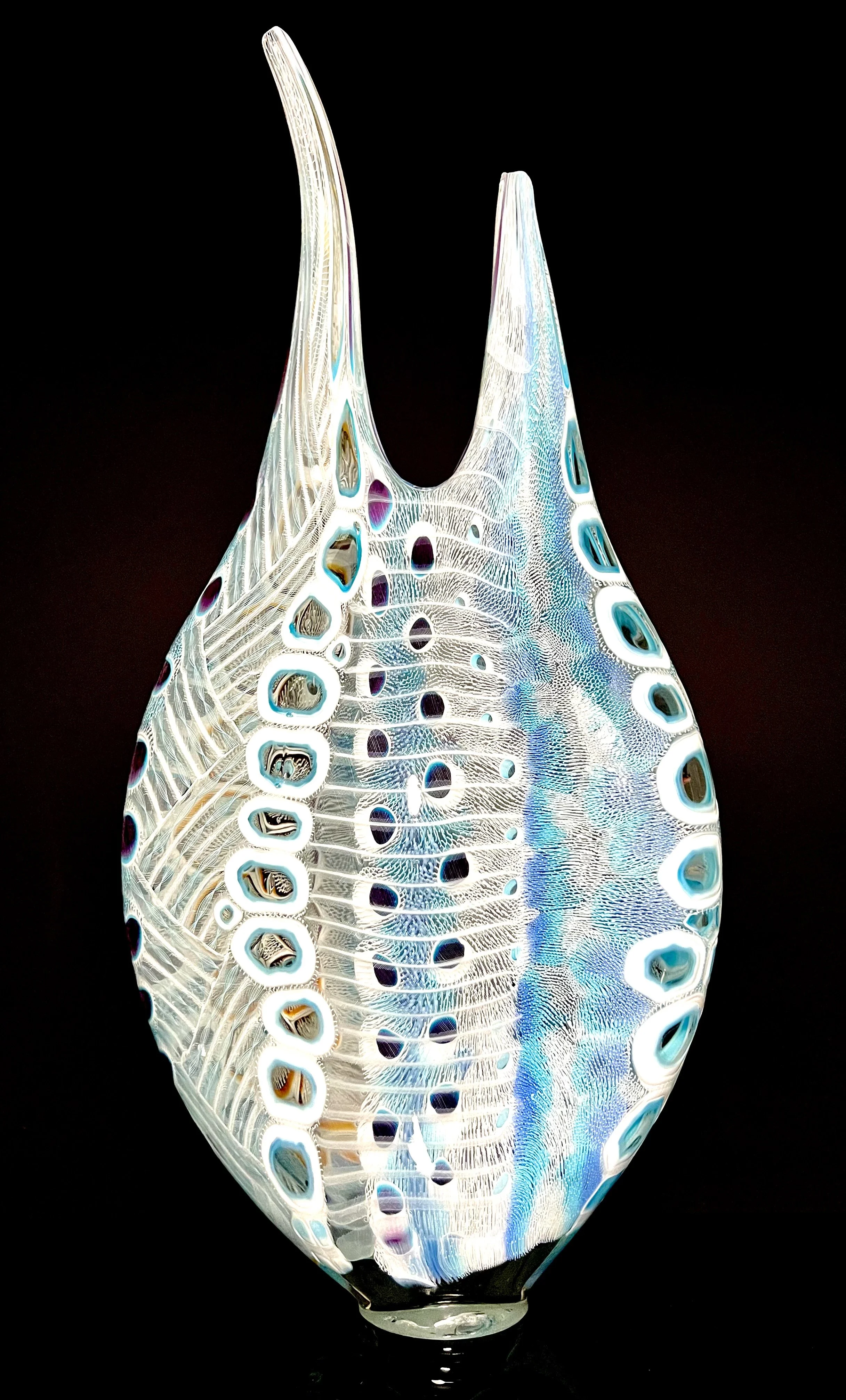 A colorful glass art sculpture with white, blue, and purple hues, resembling a shell or abstract form, set against a black background.