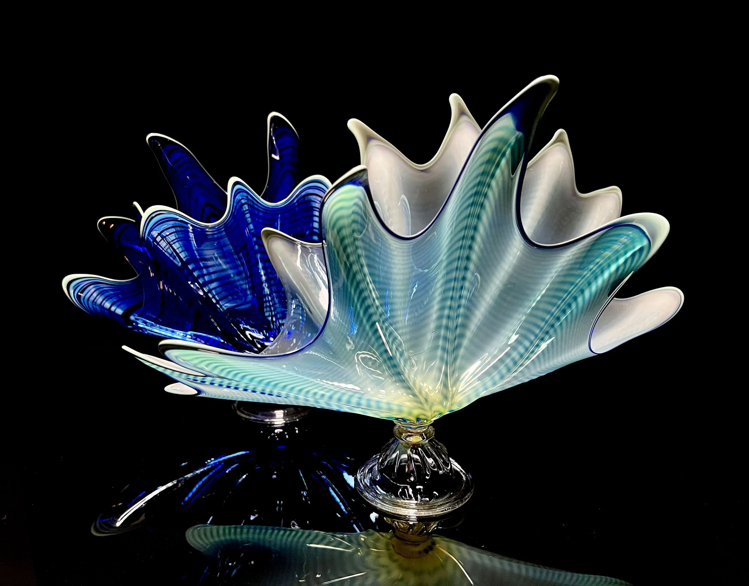 Colorful glass sculpture resembling a blooming flower with blue, white, and green shades, set against a black background.