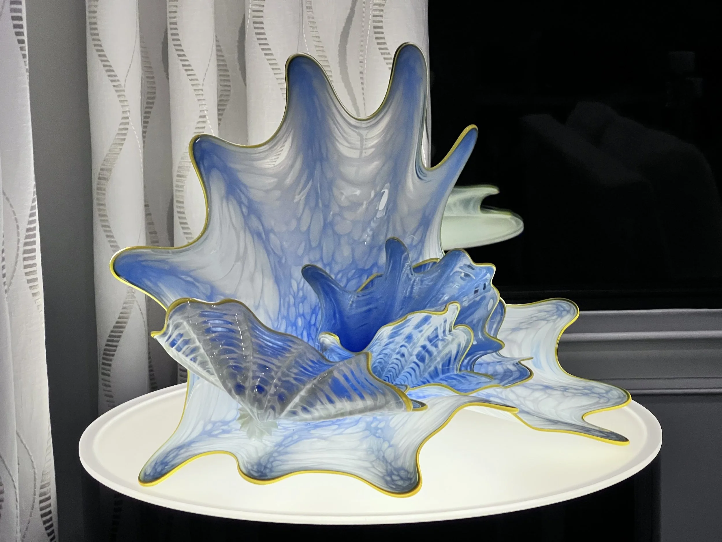 A decorative glass sculpture with blue, white, and gray marbled patterns and gold accents, sitting on a white round table.