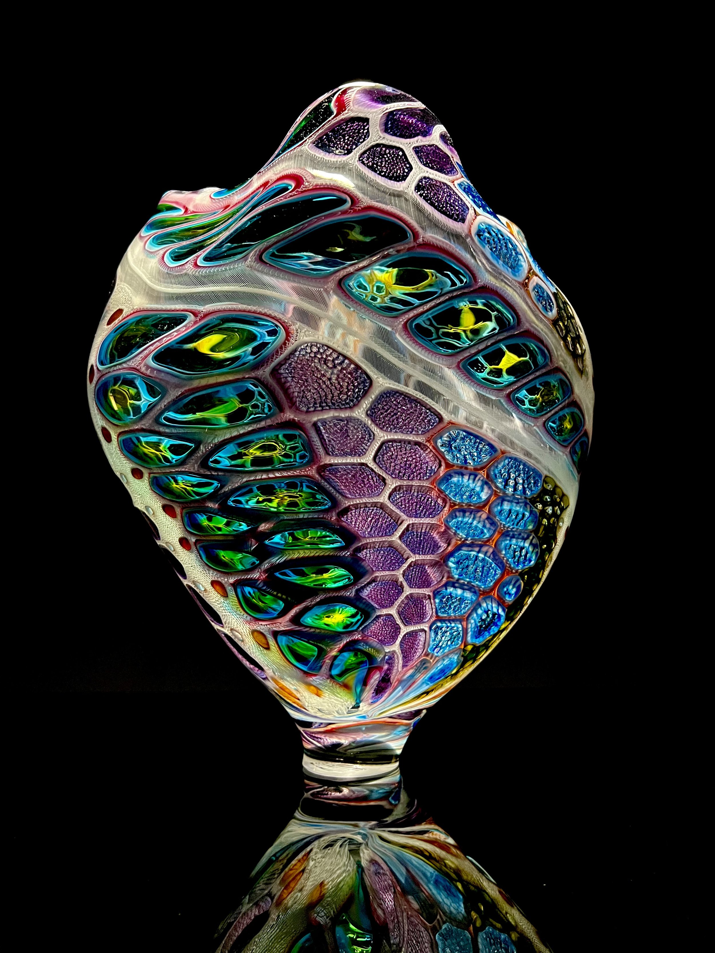 Colorful, abstract glass art piece with a honeycomb pattern, reflecting on a black surface.