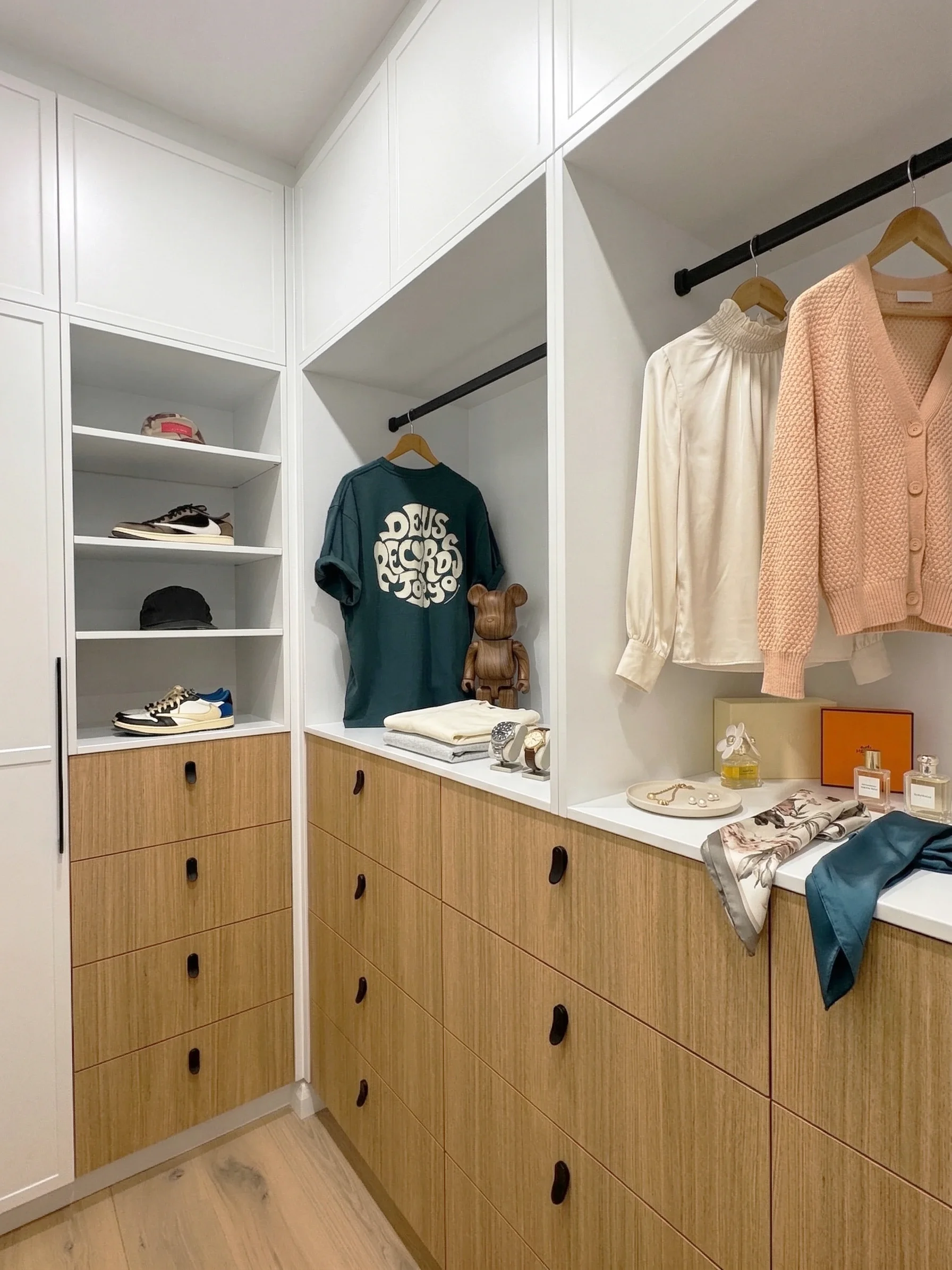 A two-toned walk-in wardrobe with white shaker doors and wooden laminate drawers with minimalist black handles. Open shelving to display bags or shoes plus open hanging space for easy access to every day clothing. Custom made by TruJoinery in Sydney