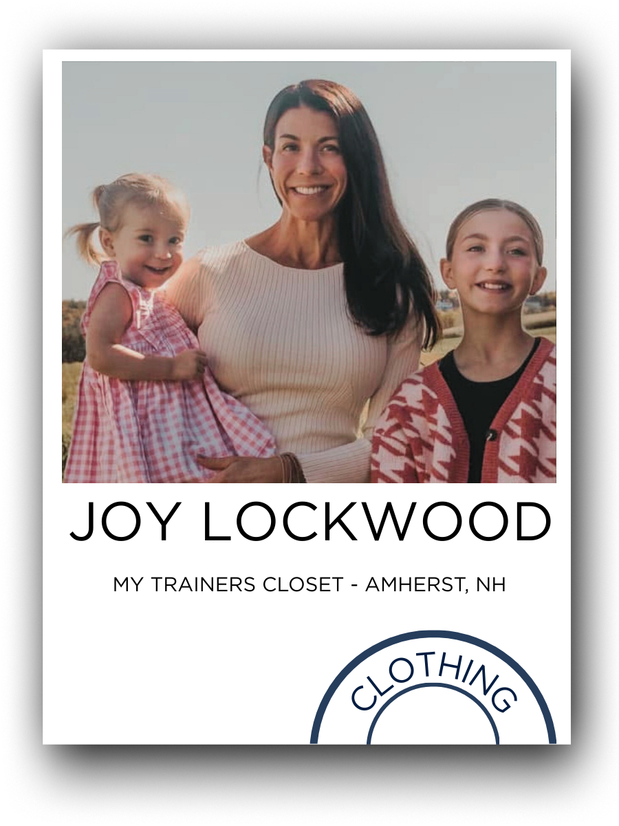 A woman smiling, holding a young girl in a pink checkered dress on her left arm, standing outdoors with another girl in a pink and white patterned jacket beside her. All are smiling, with a field in the background.