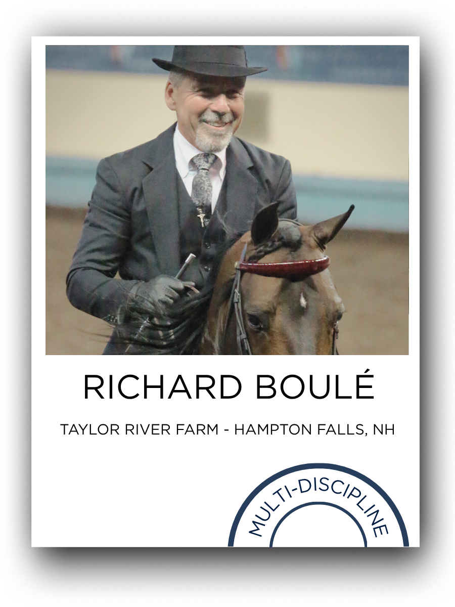 Man in a dark suit and hat riding a horse at an indoor equestrian event.