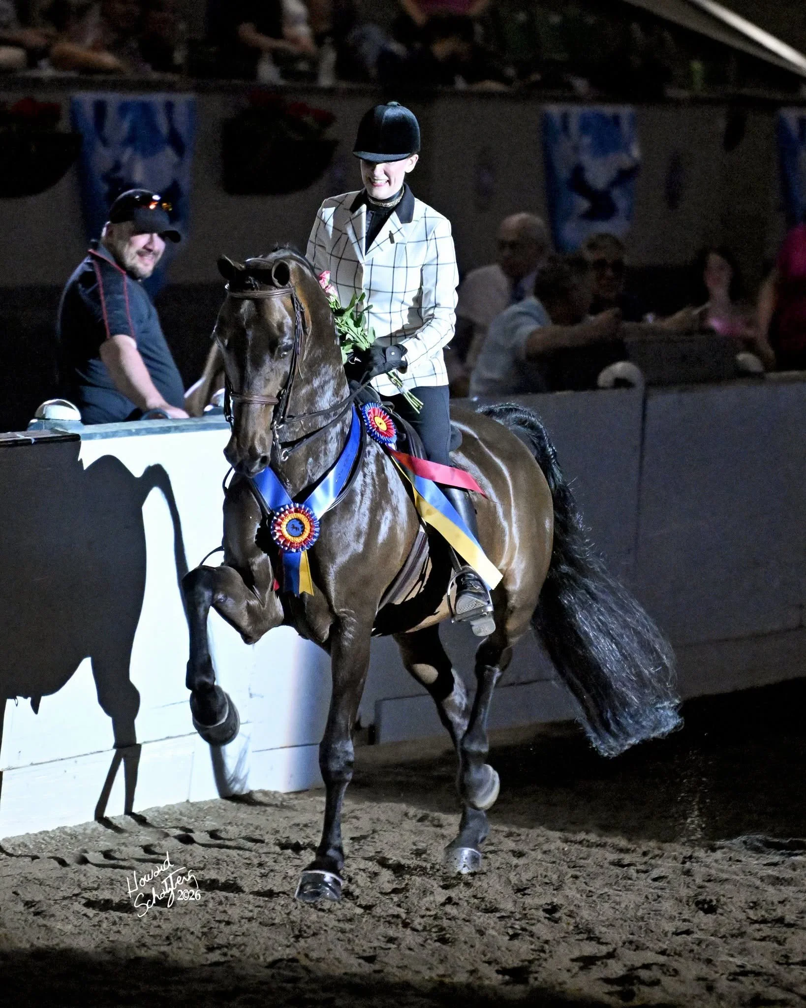 A person riding a horse during an award ceremony at a night event, with ribbons on the horse and spectators in the background.