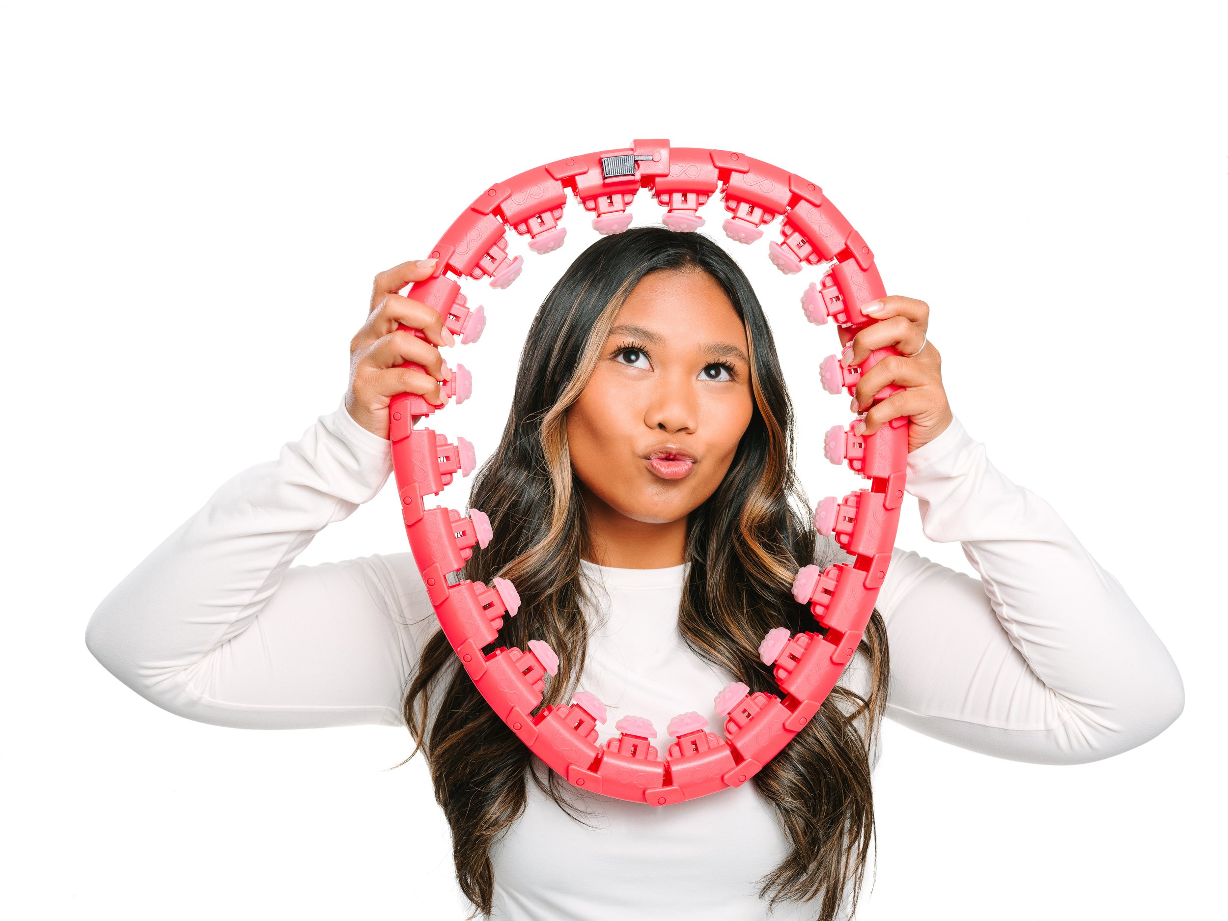 Young woman holding a pink plastic bracelet in front of her face, making a puckered lip expression.