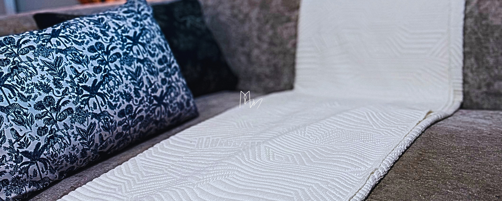 Deux coussins, l'un avec un motif floral en noir et blanc, posé sur un canapé en pierre. Devant, une nappe blanche avec un motif géométrique en relief.