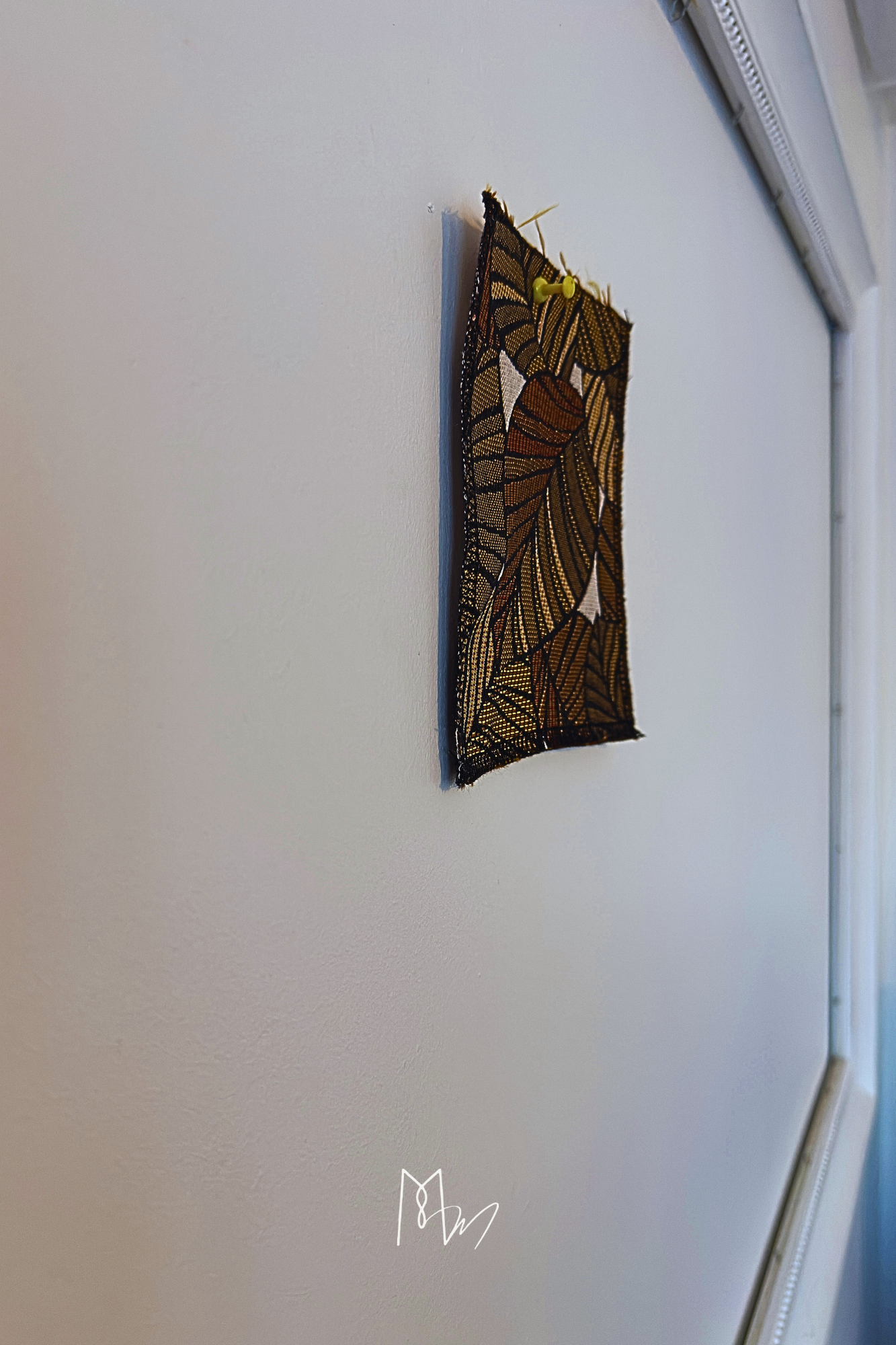 Une pièce de tissu brodé représentant un motif de feuilles d'automne, fixée au mur avec une punaise jaune.