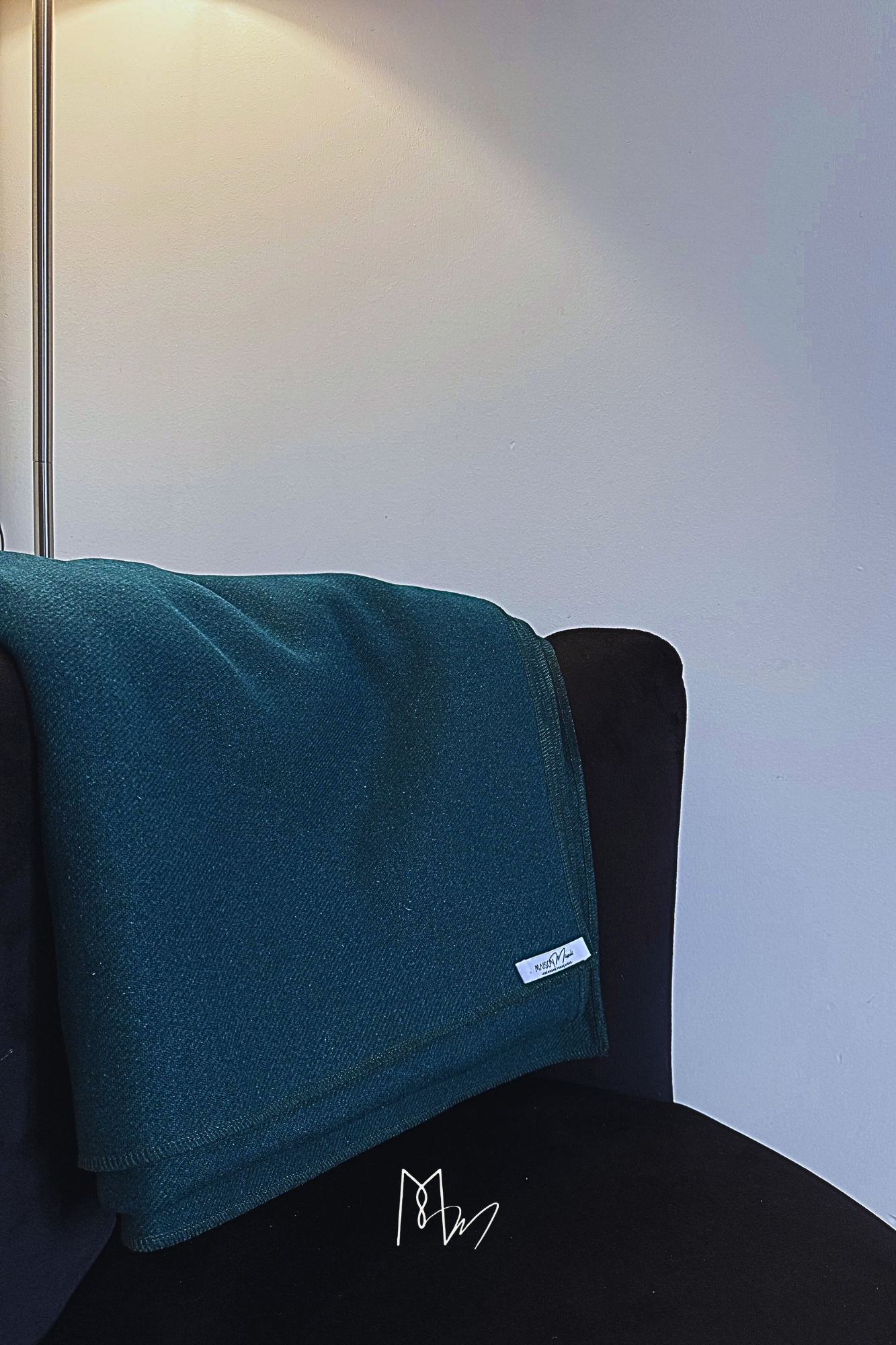 Un coussin vert foncé posé sur un fauteuil noir dans une pièce avec un mur blanc