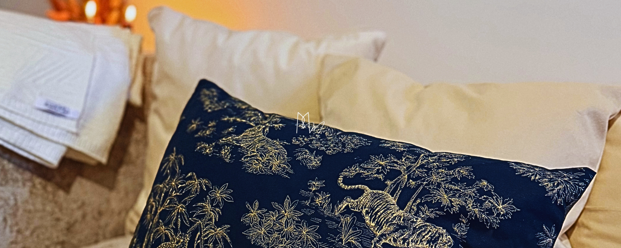 Coussin imprimé motifs animaux de la jungle : coussin de couleur bleu nuit, les imprimés de couleur jaune clair. 2 coussins velours blancs posés derrière avec un plaid écru, posés sur un canapé.