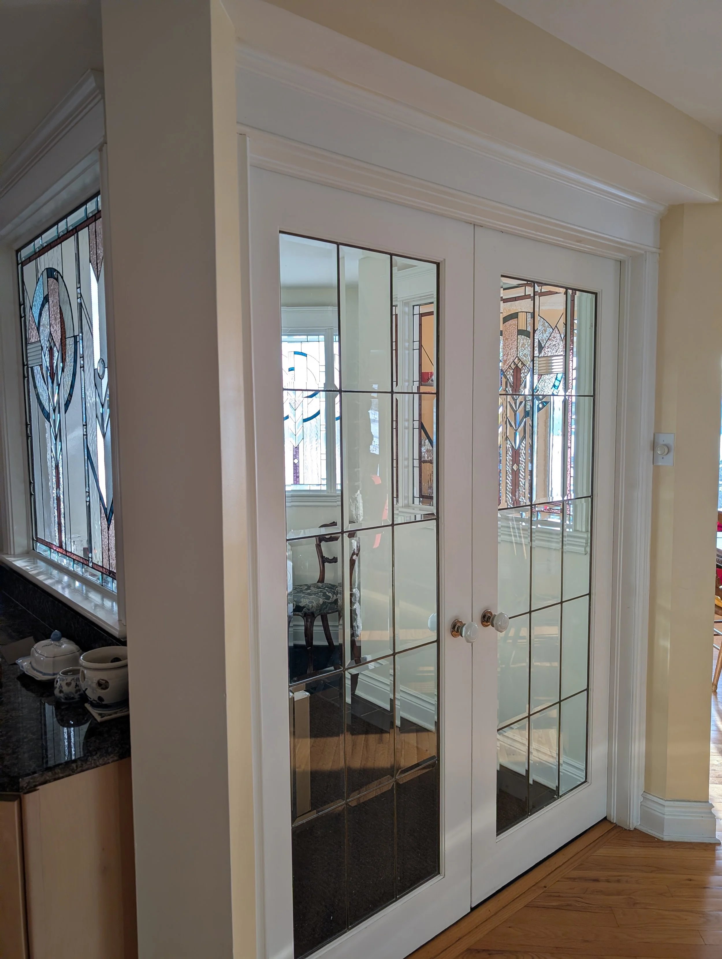 White double glass doors with grid panes in a room with stained glass windows, a chair, and hardwood floors.